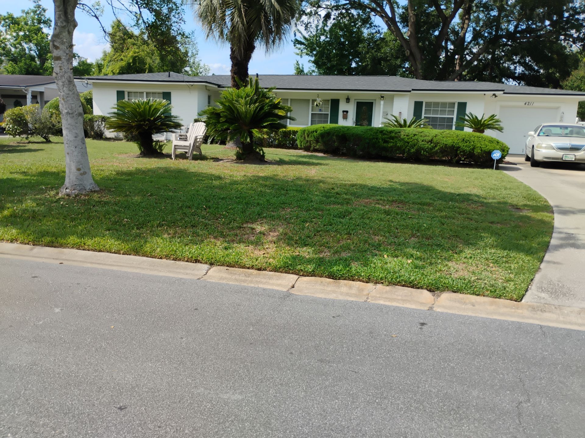Single-story suburban house with a green lawn, palm tree, and driveway with parked car.