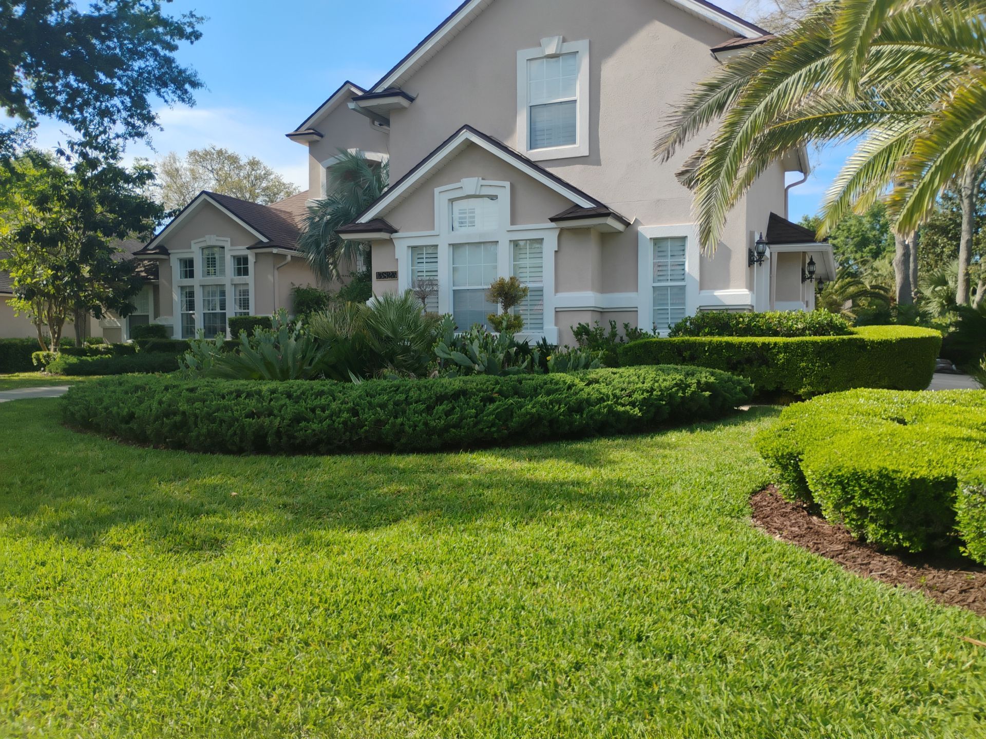 Large beige house with white shutters and manicured green lawn under a sunny sky