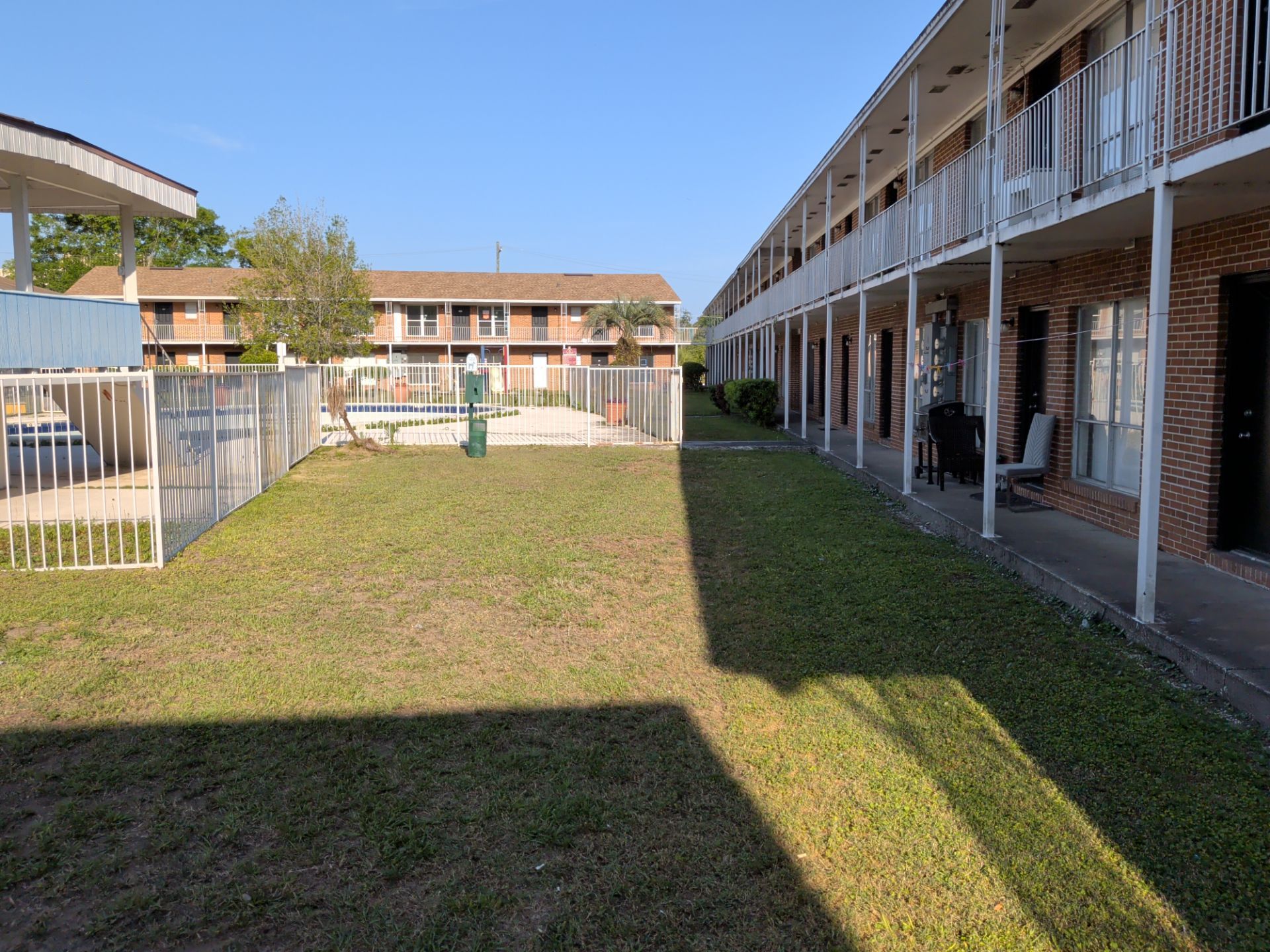 Courtyard between brick apartment buildings with grassy lawn and covered walkways in sunlight