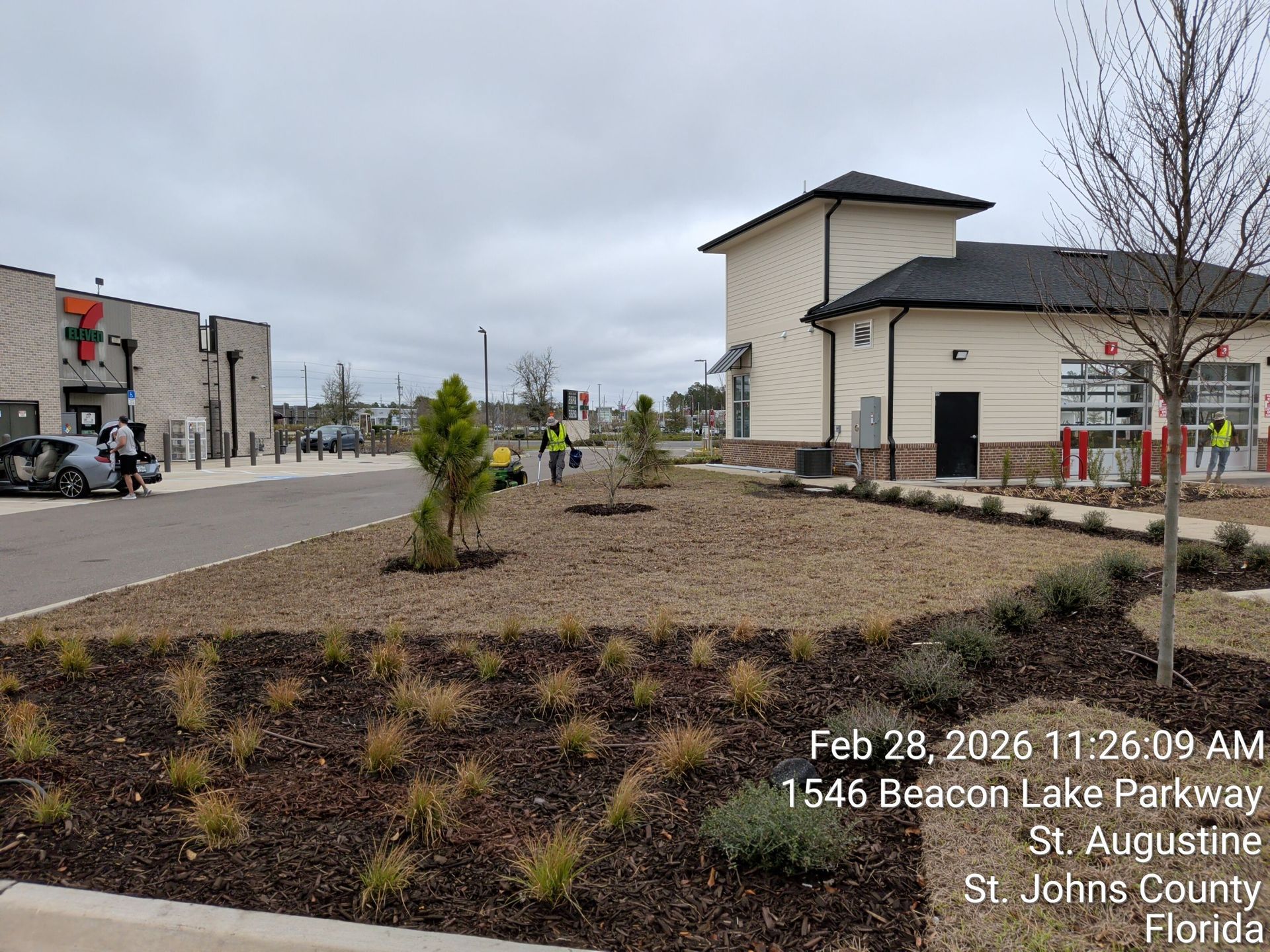 Landscaped median beside a street with buildings under a cloudy sky.