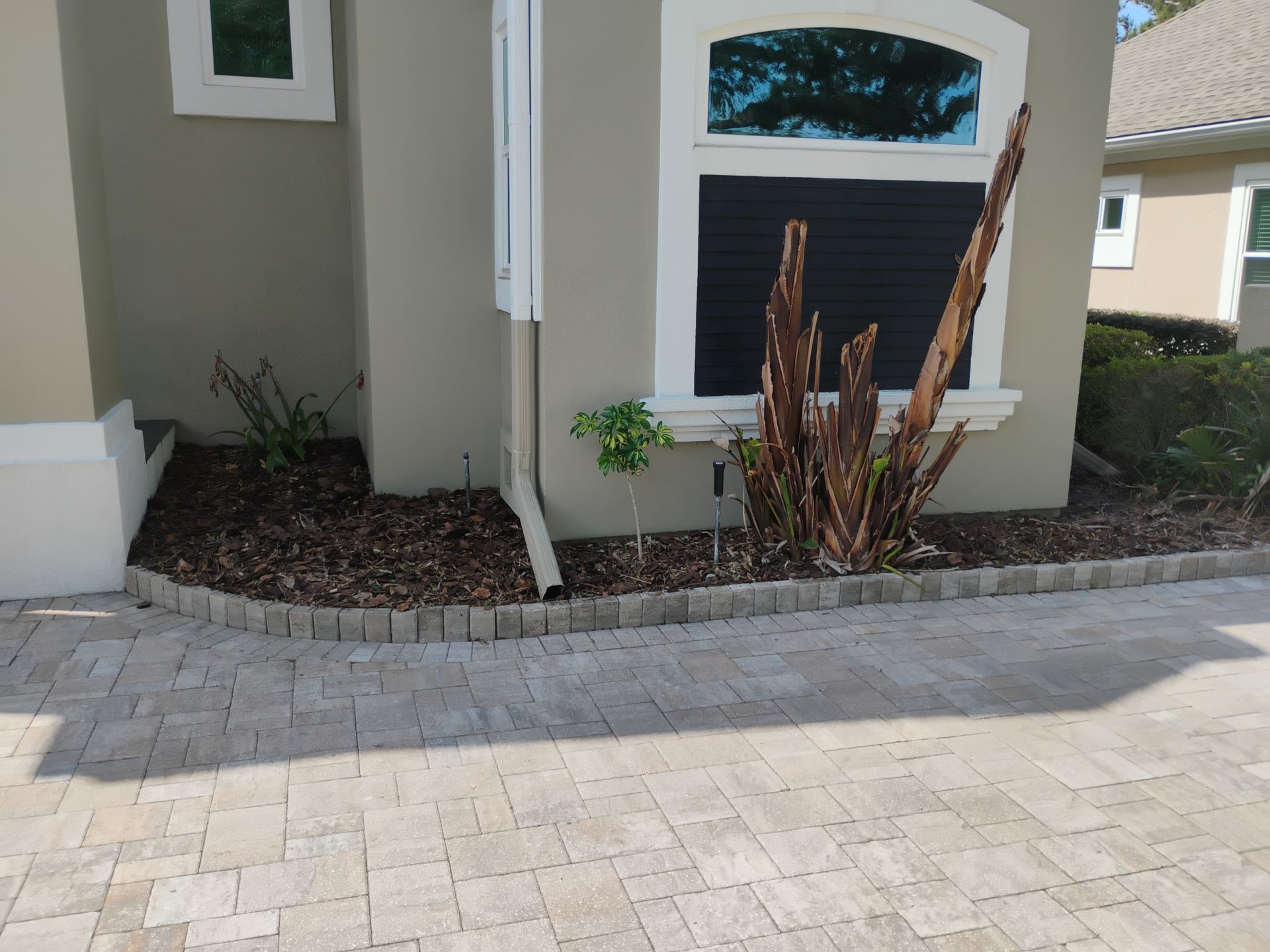 Front entrance of a house with paver driveway, gray walls, white trim, and sparse landscaping