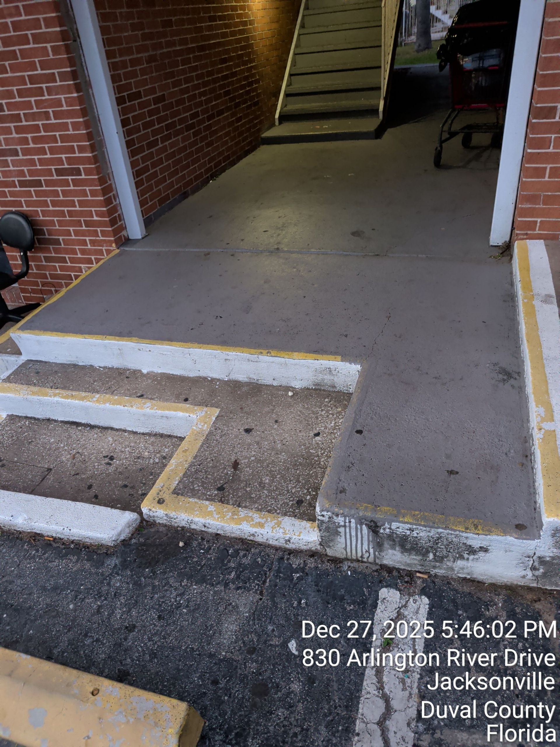 Accessible sidewalk ramp with yellow edge markings leading to a brick building entrance