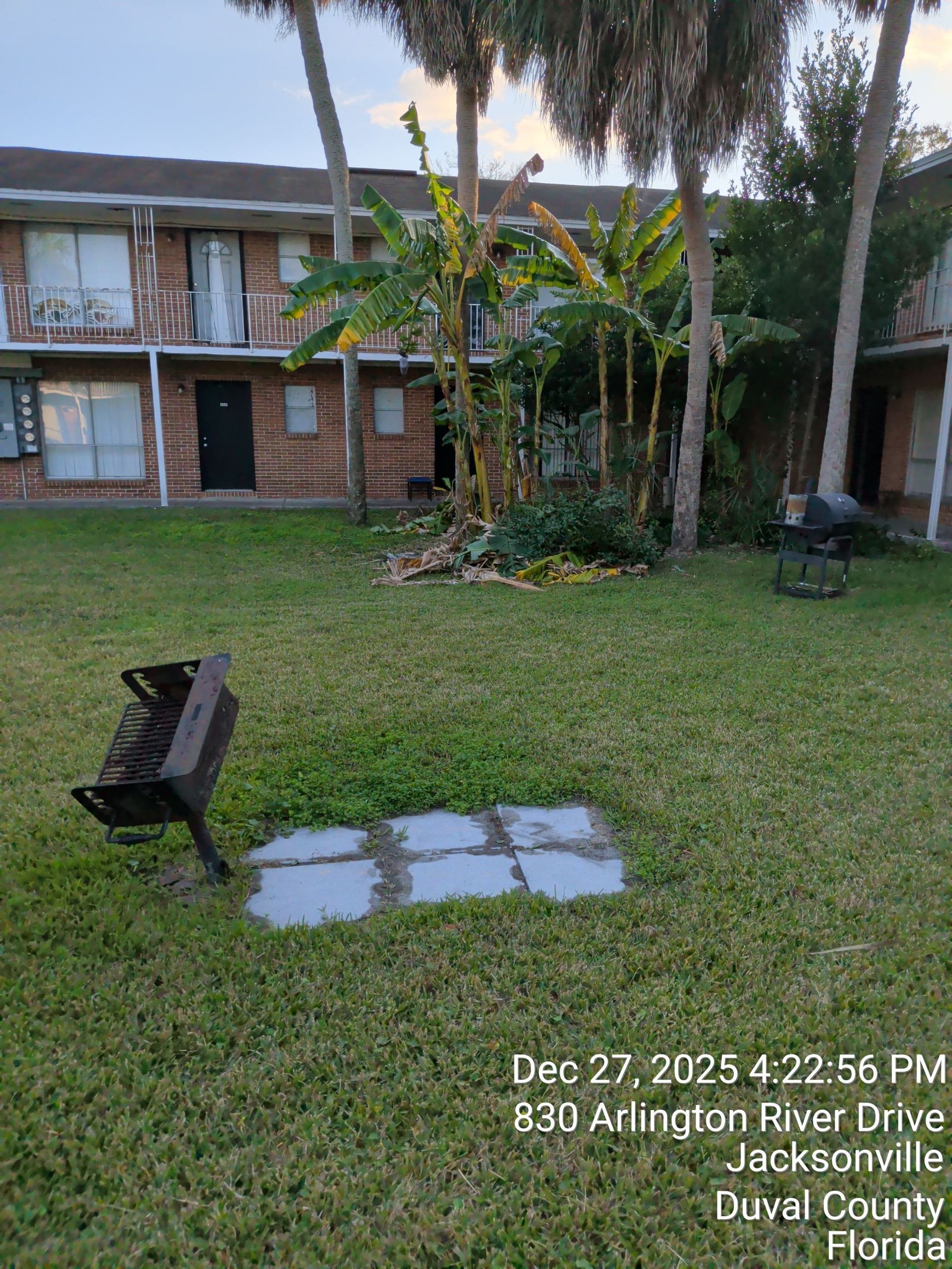 Rain-soaked motel courtyard with benches, banana trees, and puddles after dusk