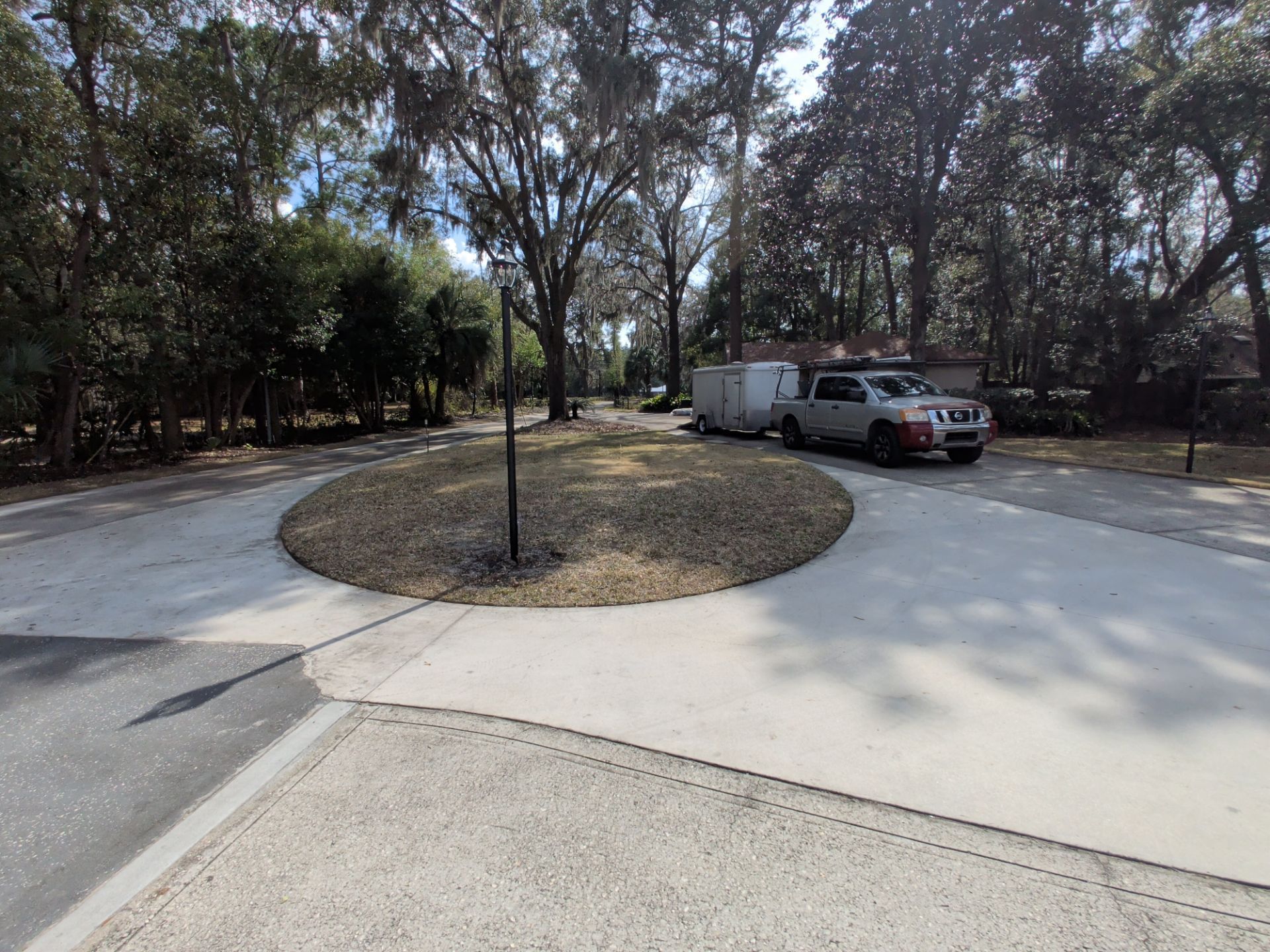 Curved driveway around a tree island, with a parked truck and van beside a wooded area.