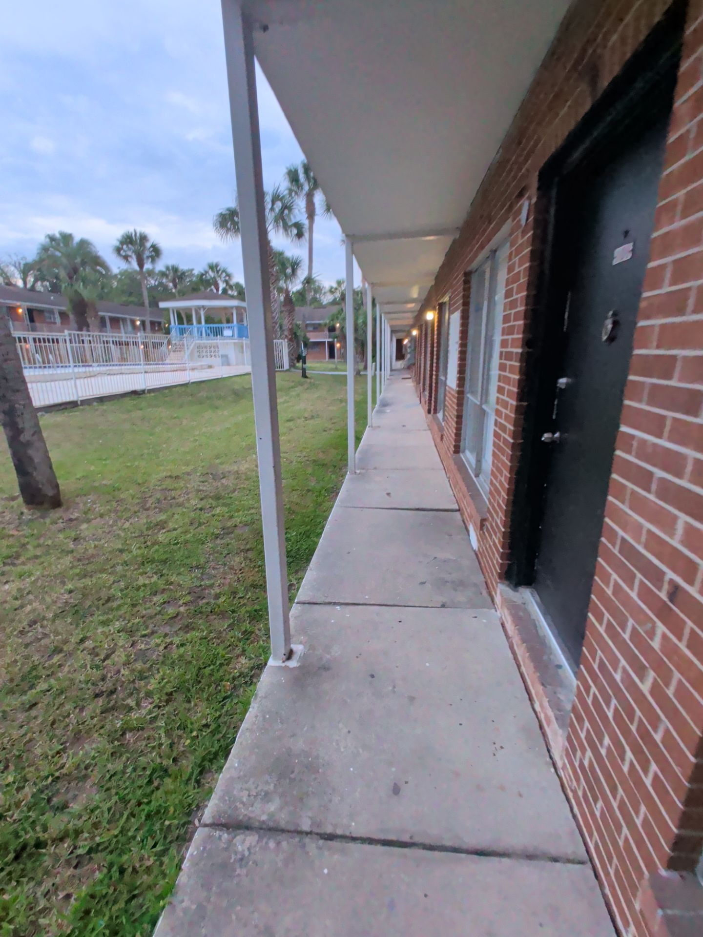Brick motel walkway with doors and support posts beside a grassy pool area