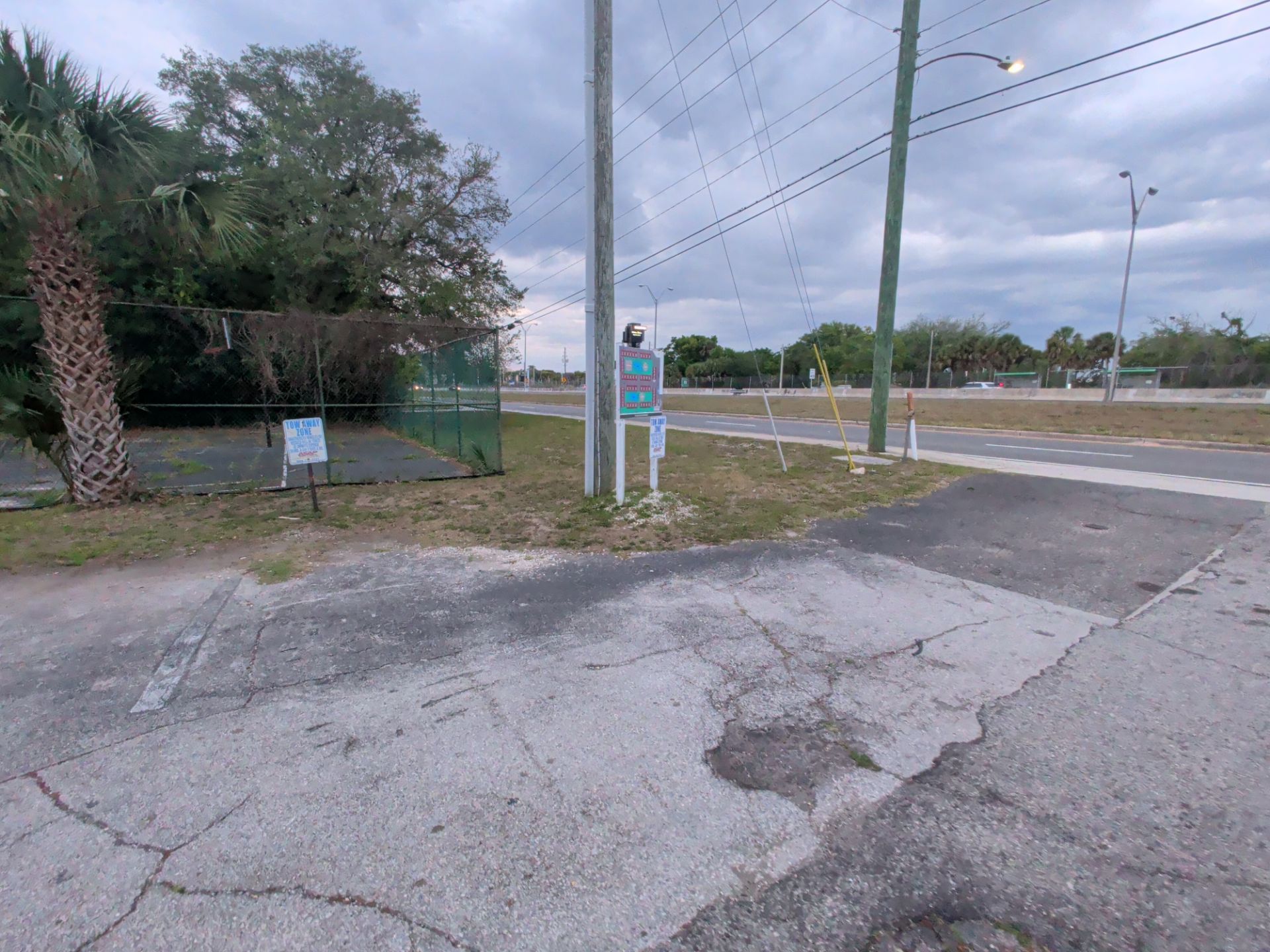Cracked paved lot beside a roadside intersection with utility poles, a sign, and overcast sky