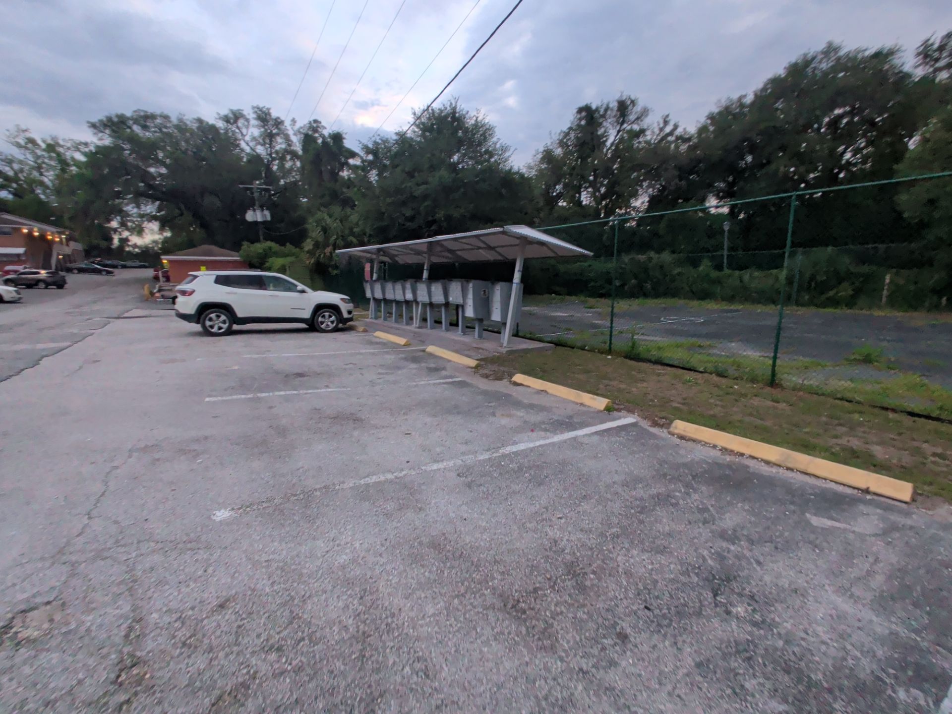 Empty parking lot with a white SUV near a covered shelter and chain-link fence at dusk
