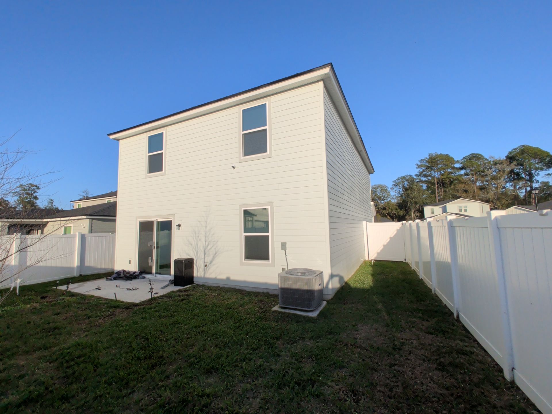Backyard view of a two-story white house with a fenced yard and patio.