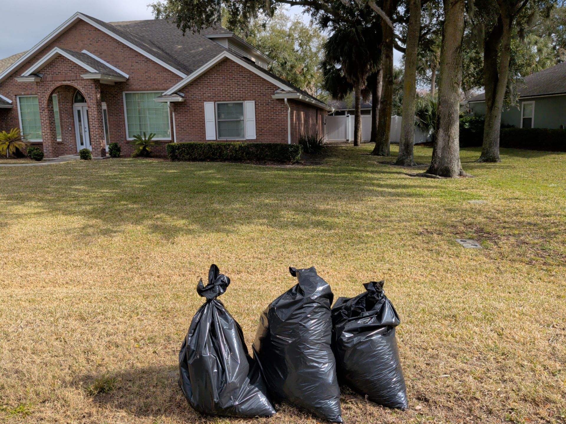 Three black trash bags on a grassy lawn in front of a brick house