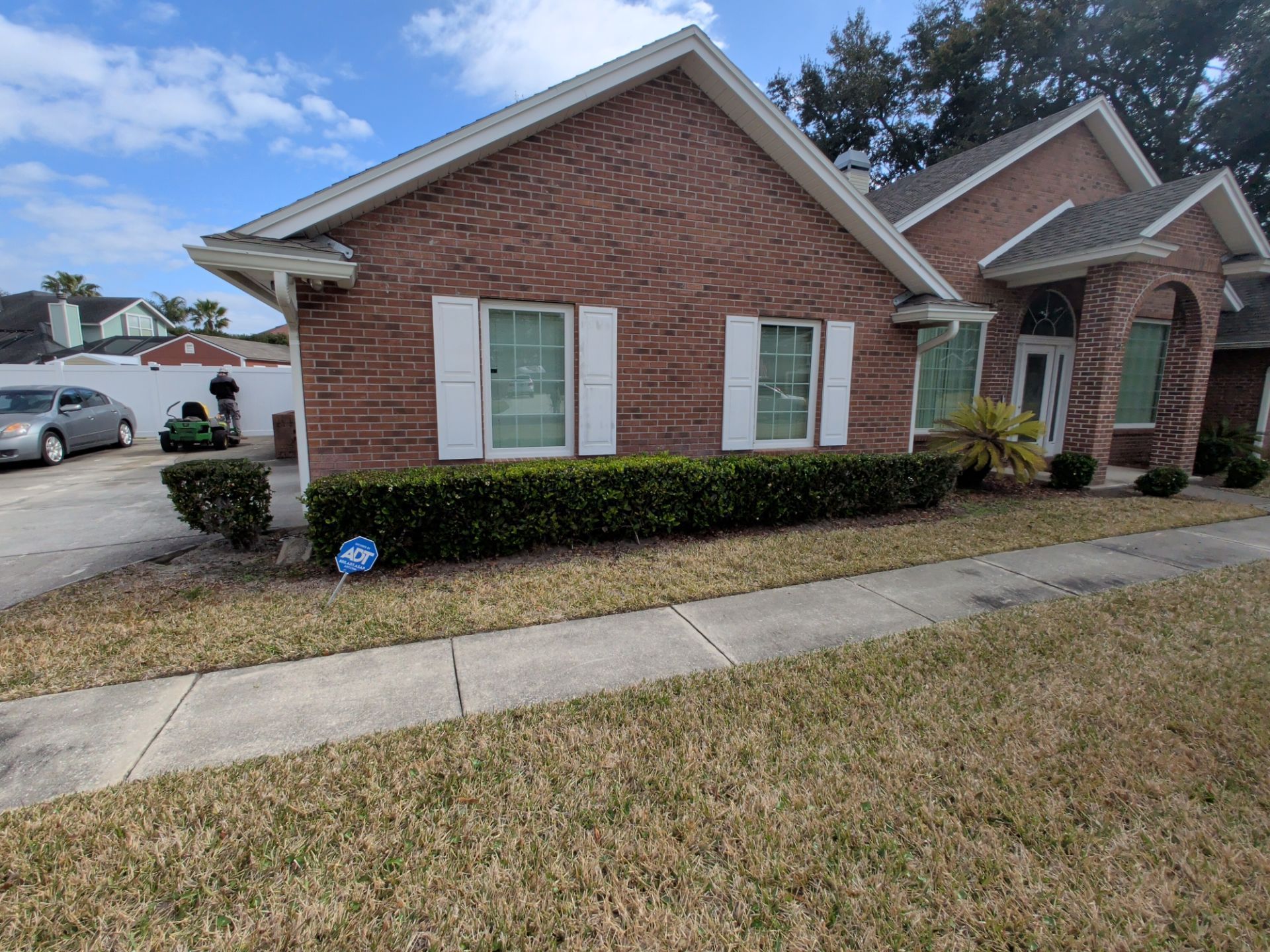 Brick suburban house with white shutters, trimmed hedge, and sidewalk at the front yard