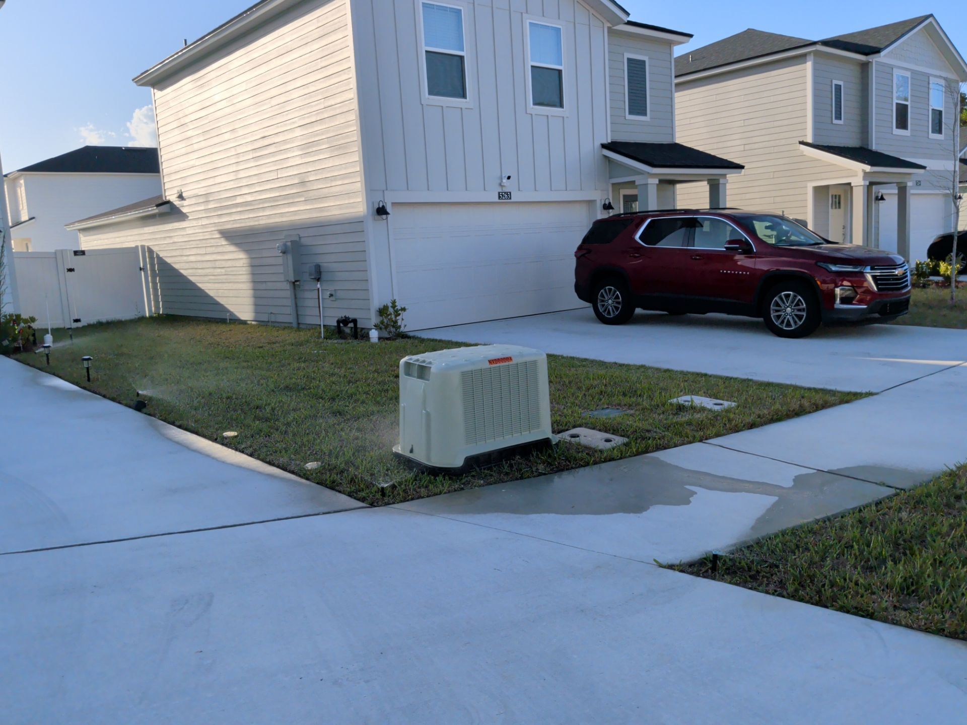 Suburban house with a red SUV parked in the driveway and a utility box on the lawn.
