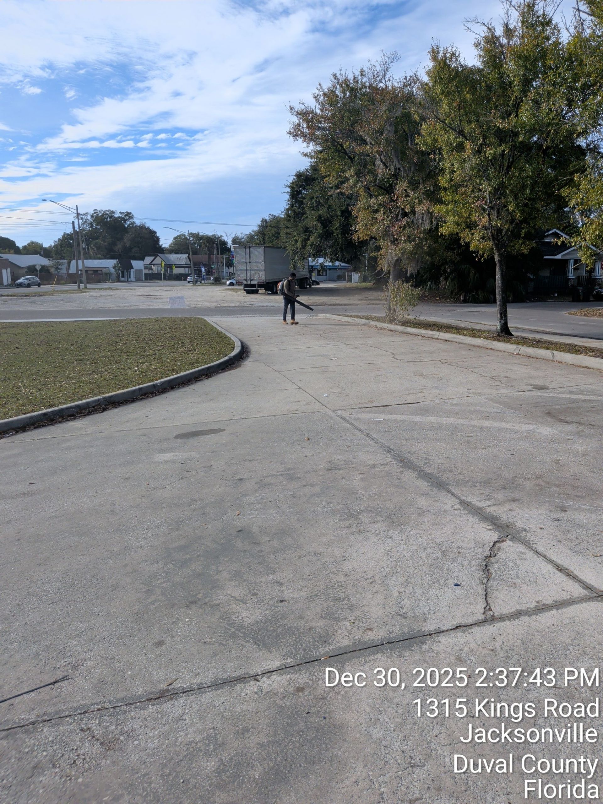 Curved park path with a person walking in the distance, trees, grass, and a cloudy sky