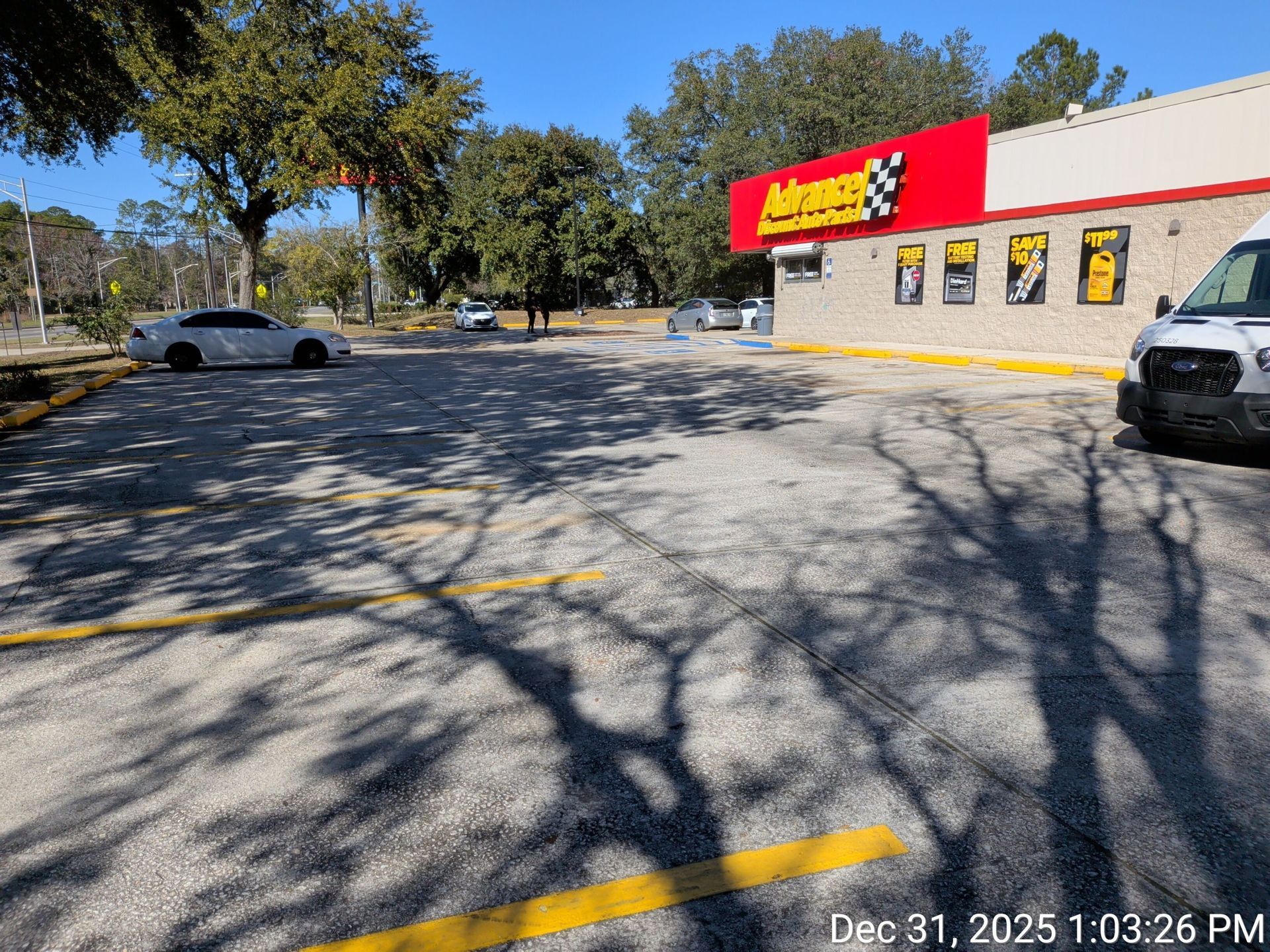 Parking lot in front of an AutoZone store. Sunny day, shadows on pavement, cars parked.