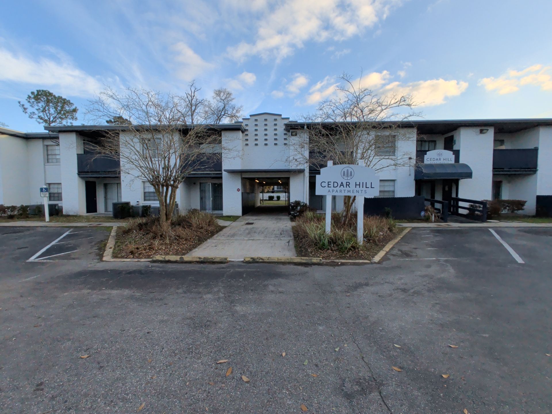 Apartment building entrance with parking lot, trees, and a cloudy sky at dusk