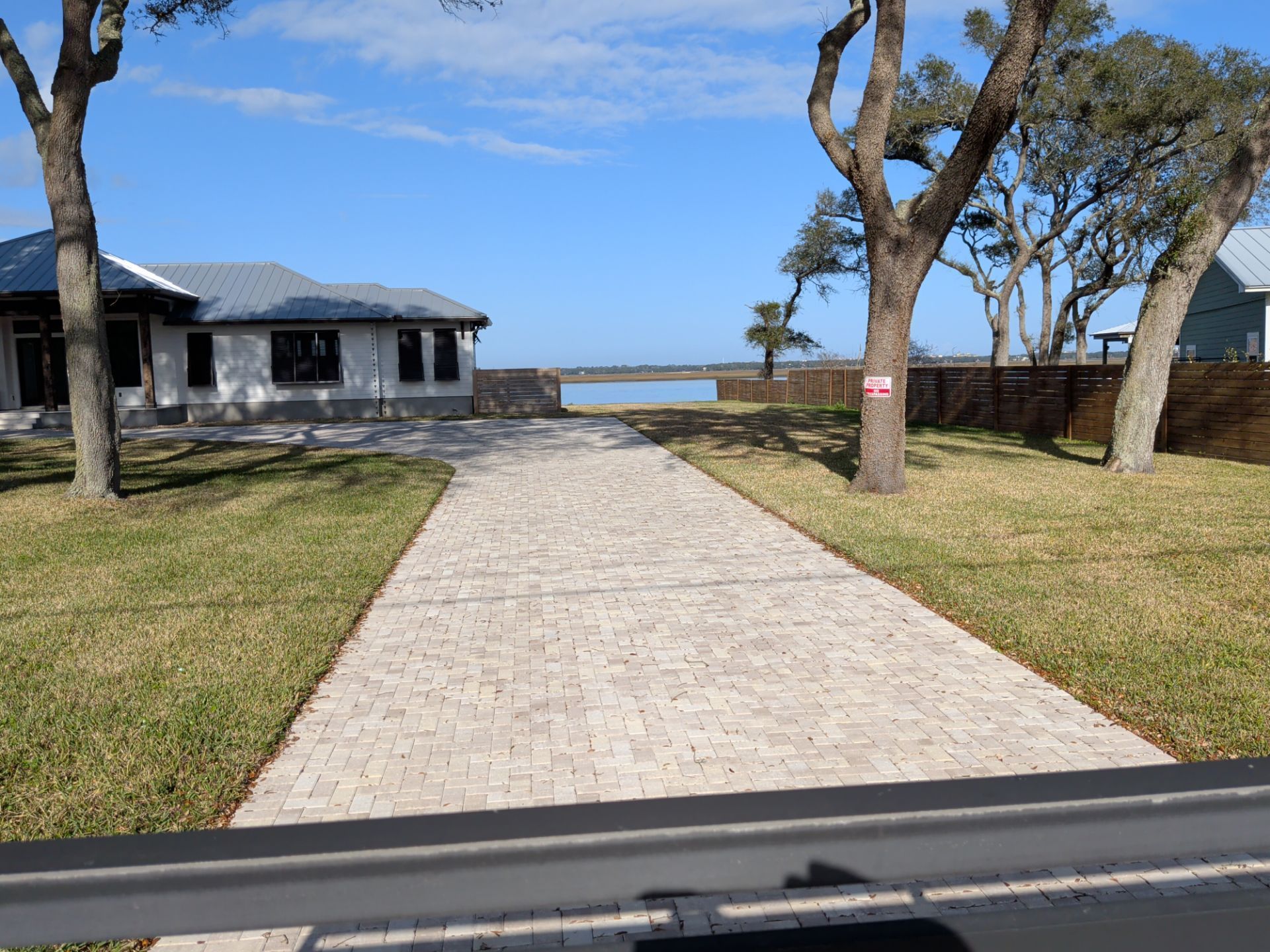 Stone walkway leading to a waterfront building, with trees, grass, and blue sky.