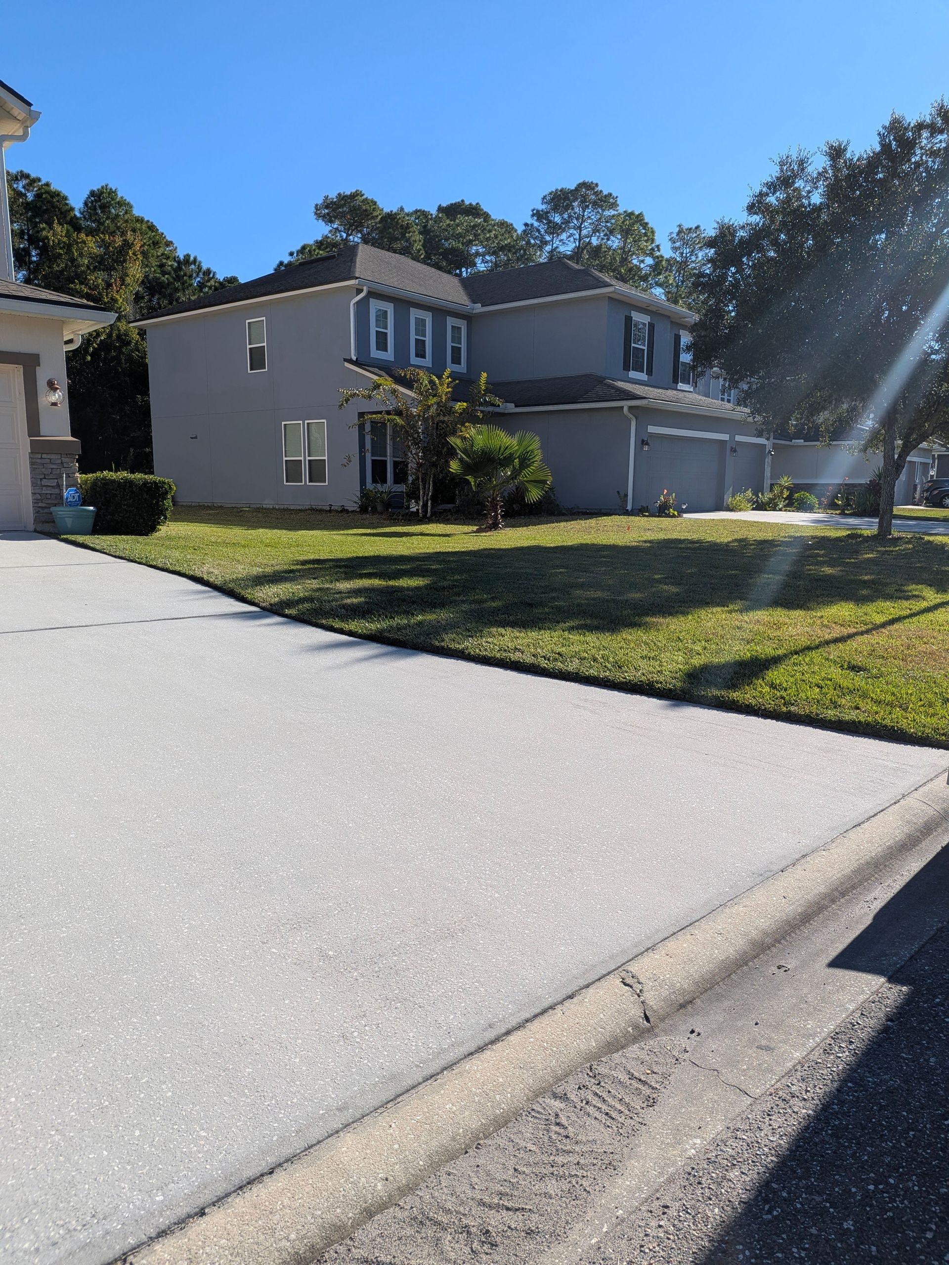 Suburban two-story house with driveway, lawn, and bright sunlight