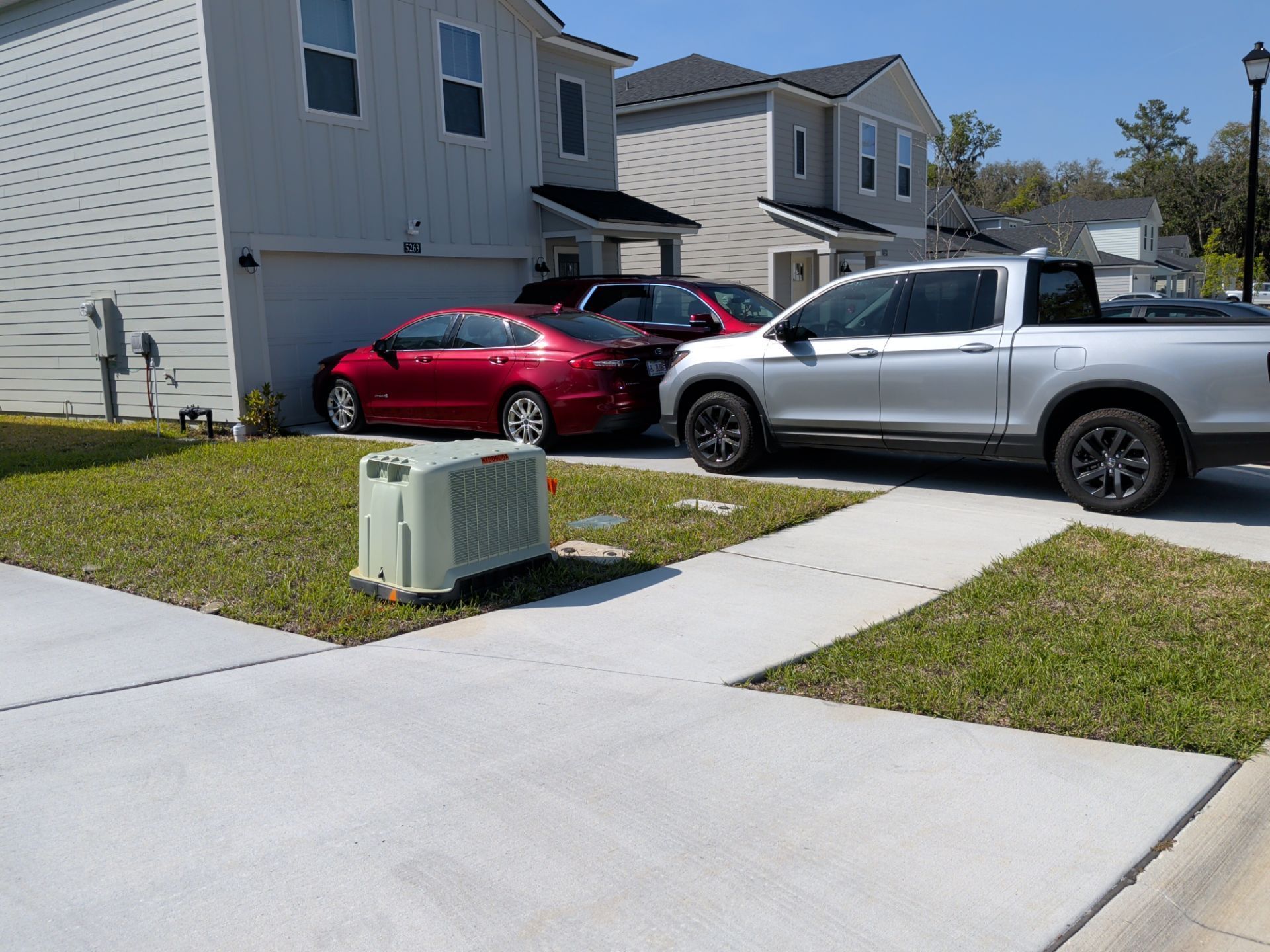 Suburban driveway with a red car and silver pickup parked beside a house and utility box