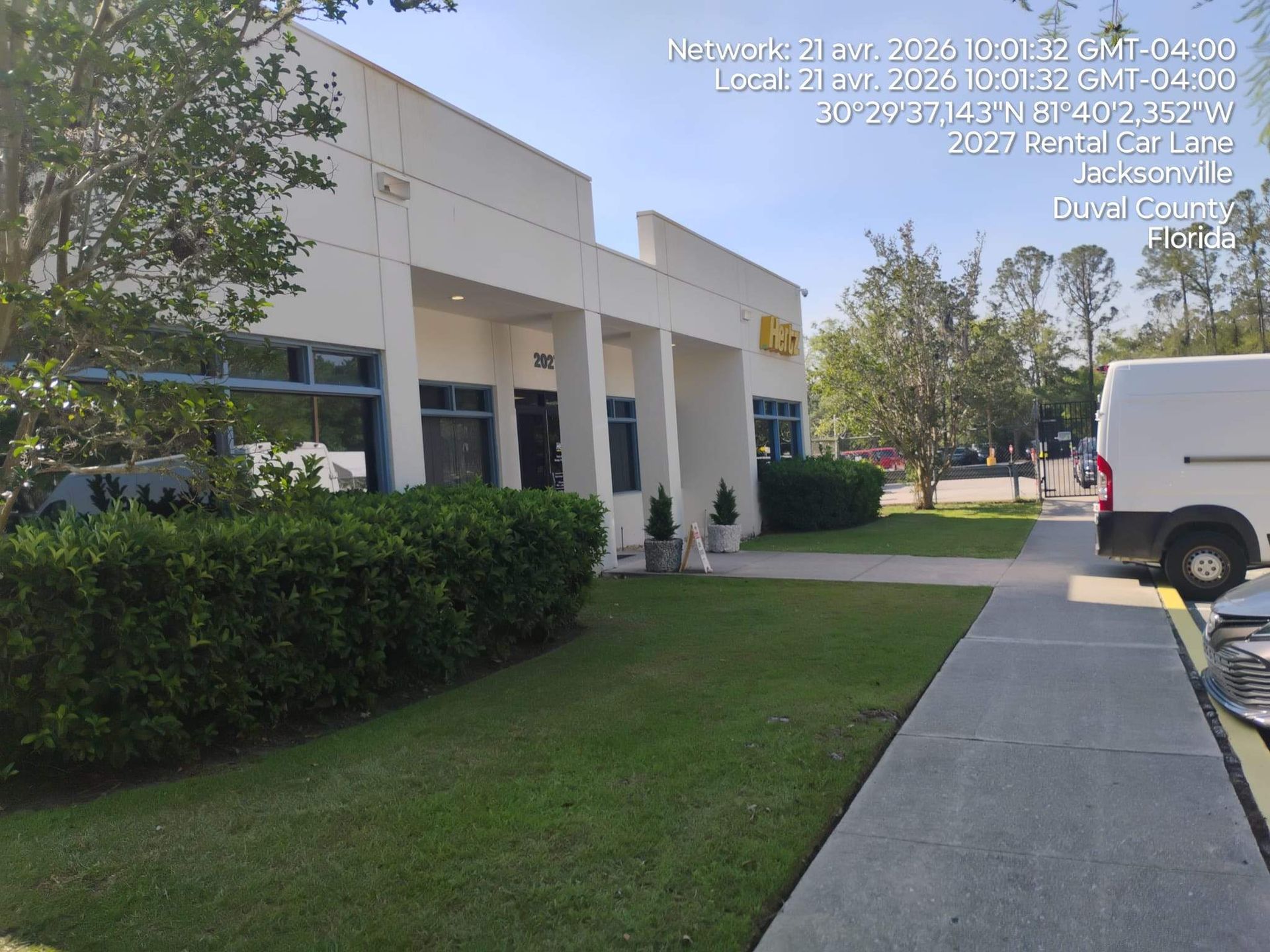 Office building with hedge-lined sidewalk, green lawn, and a white van parked along the curb