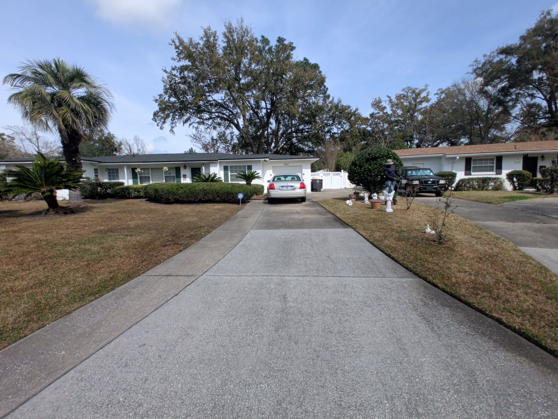 Driveway leading to a single-story suburban house with a white SUV parked in front and a person near the right side.