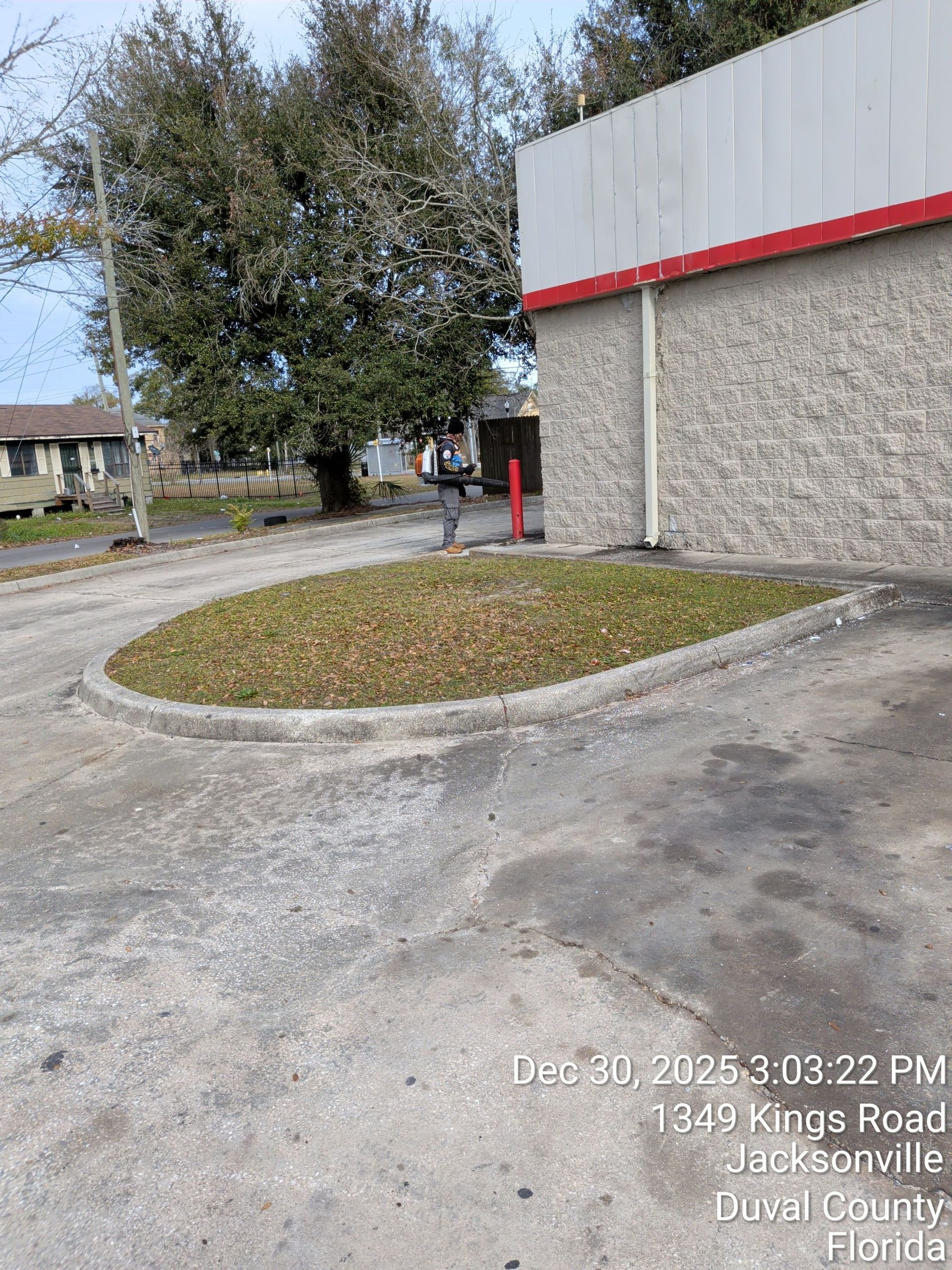 Empty drive-through lane beside a gray building with a red stripe and a tree-lined curb island