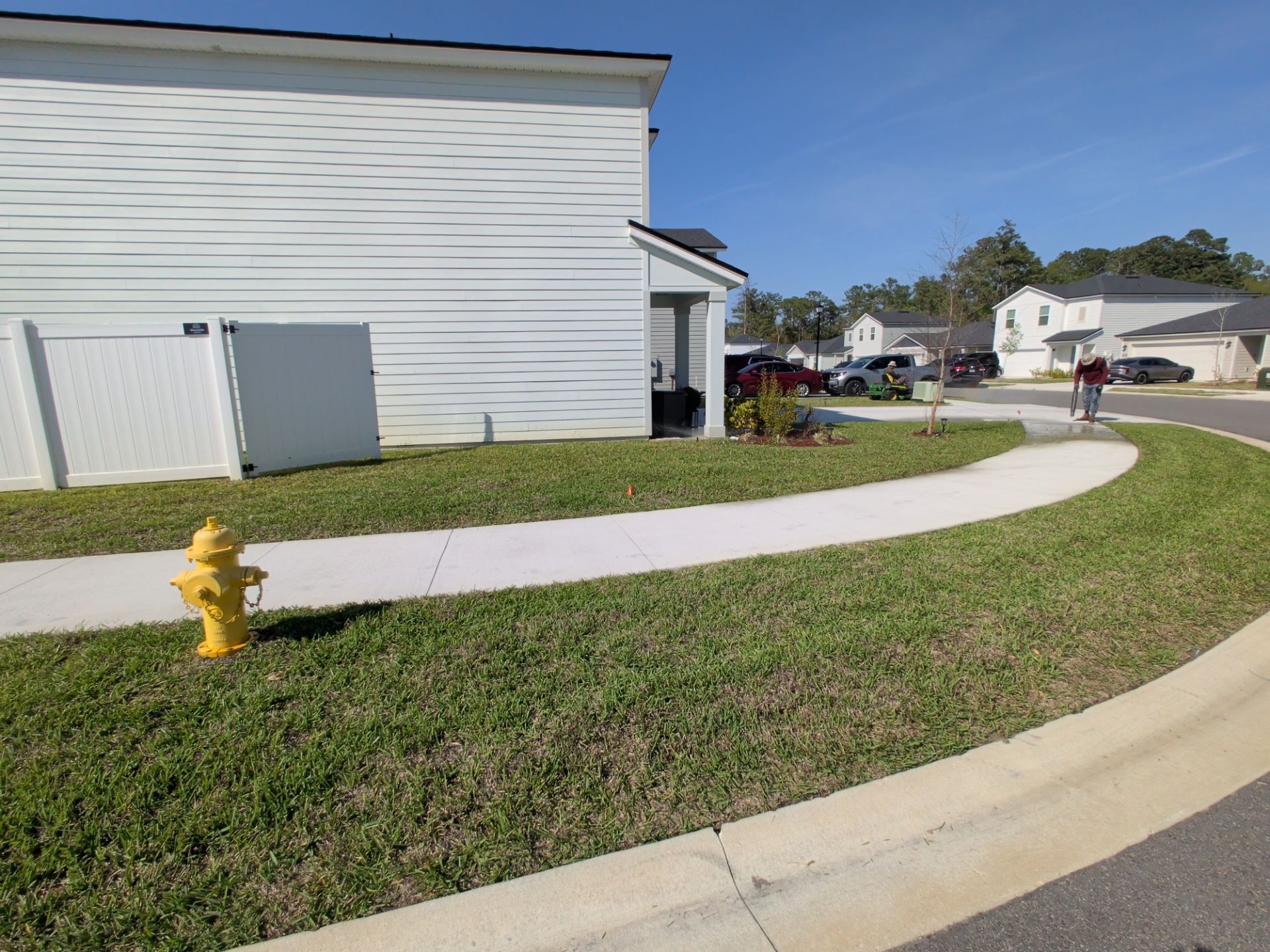 Curved sidewalk beside a white building, with a yellow fire hydrant and houses in the background.