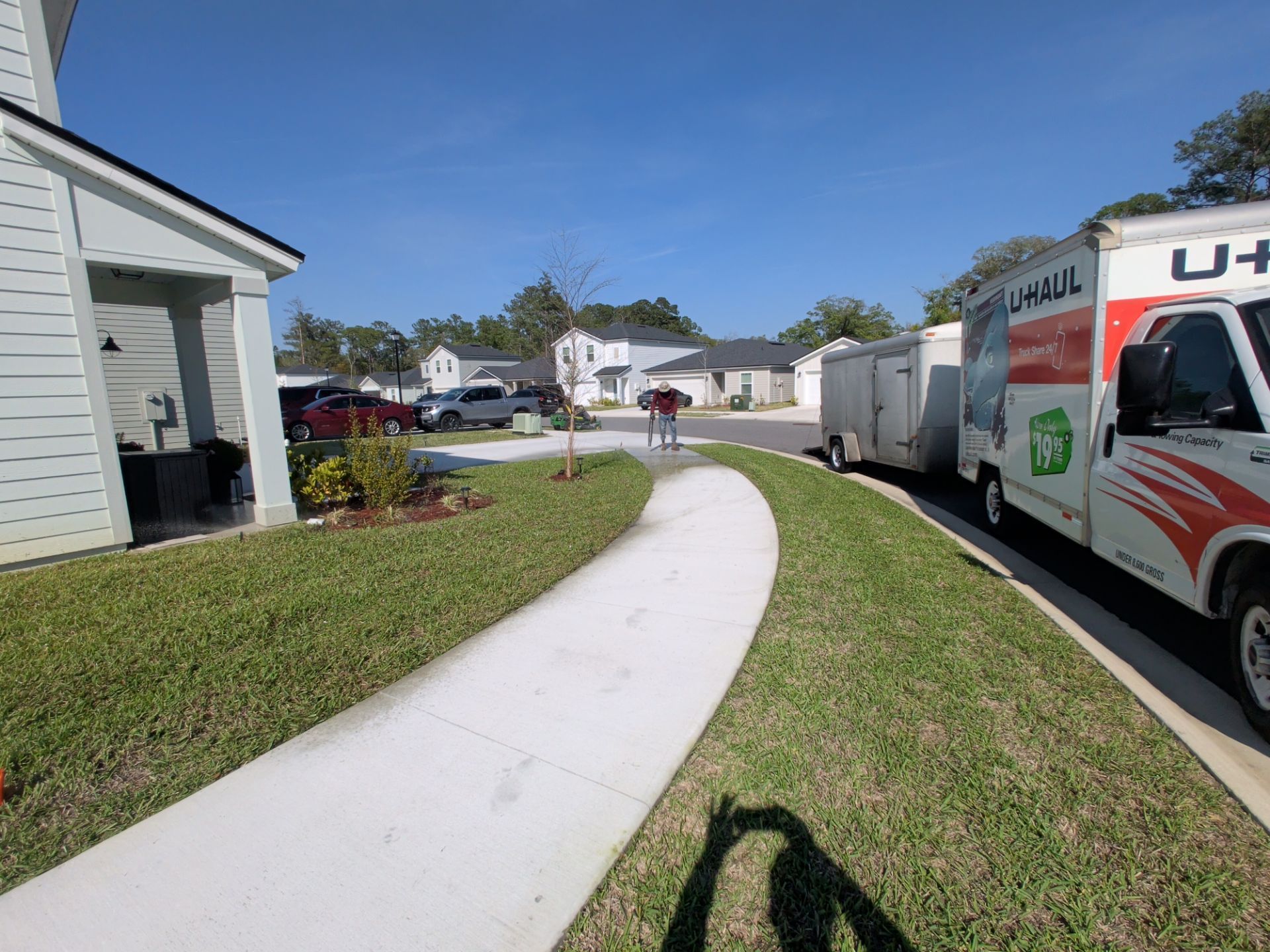 Suburban sidewalk beside a house and moving truck on a sunny day, with a shadow in the foreground