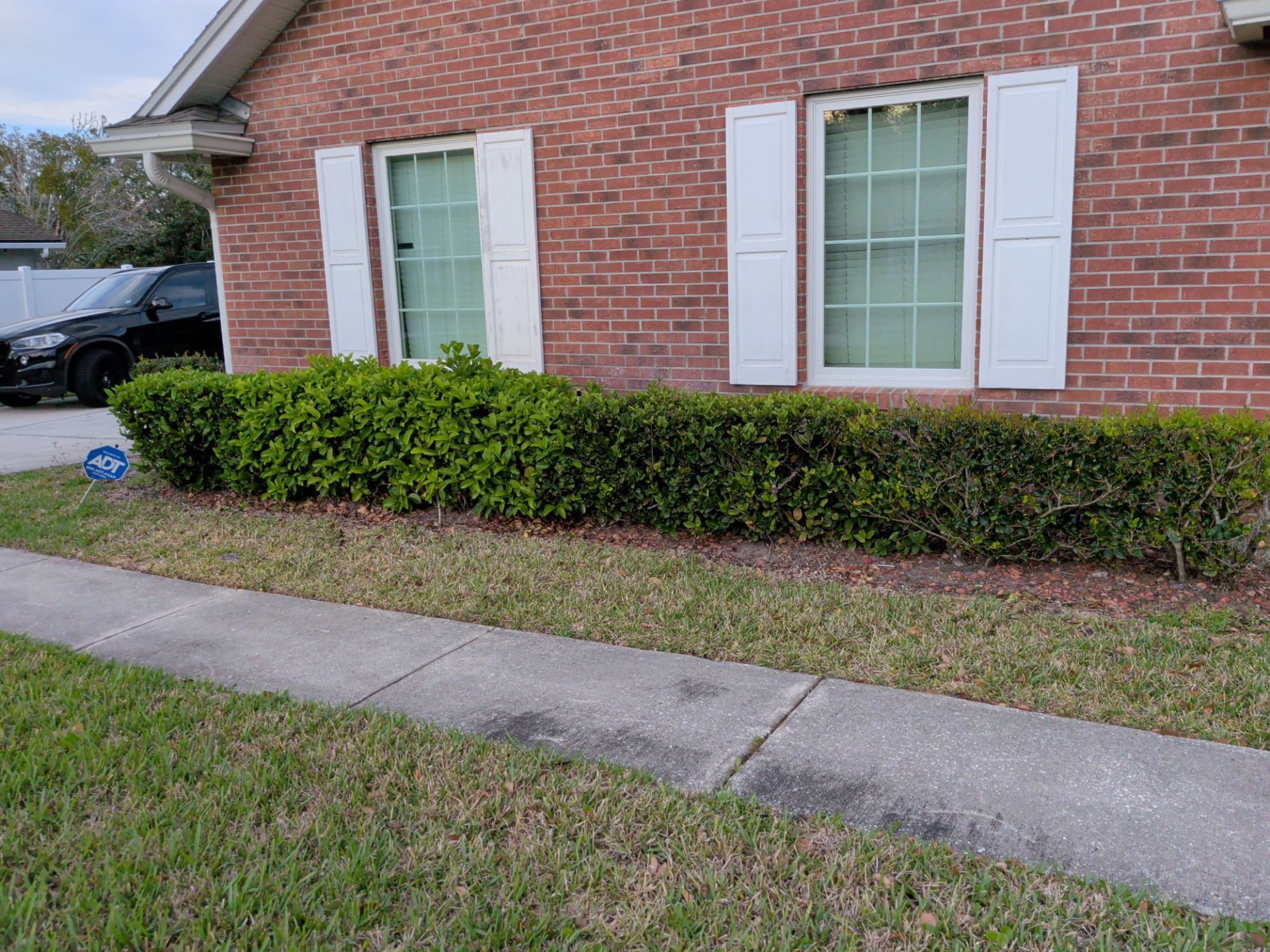 Brick house exterior with white shutters, trimmed hedges, and a sidewalk in front
