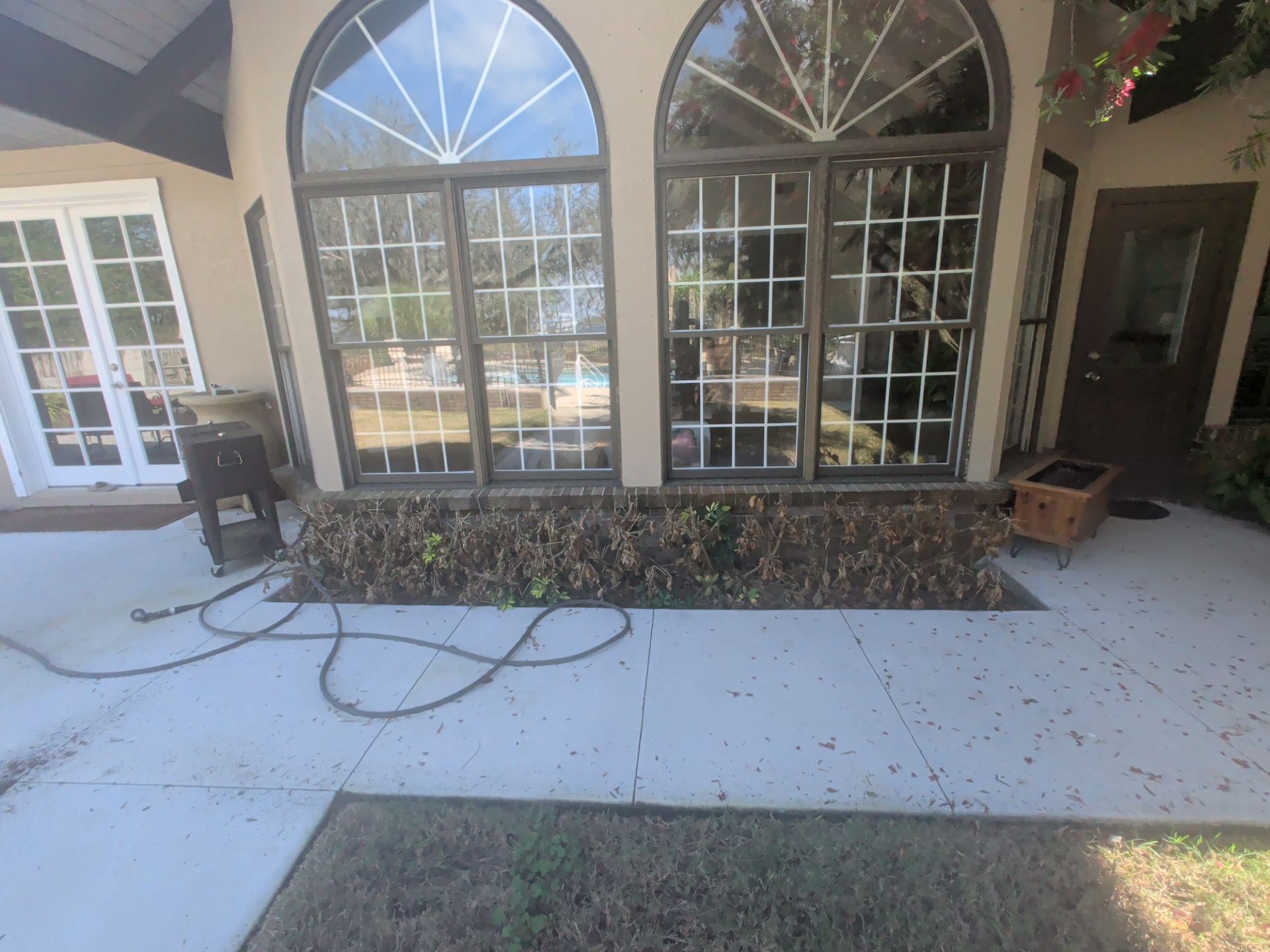 Patio with arched windows, patio furniture, and a coiled hose on a sunlit concrete floor