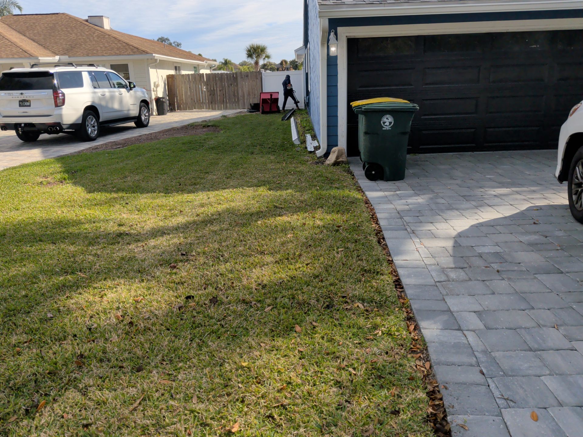 Suburban driveway with a black garage door, green trash bin, parked van, and a narrow grassy strip