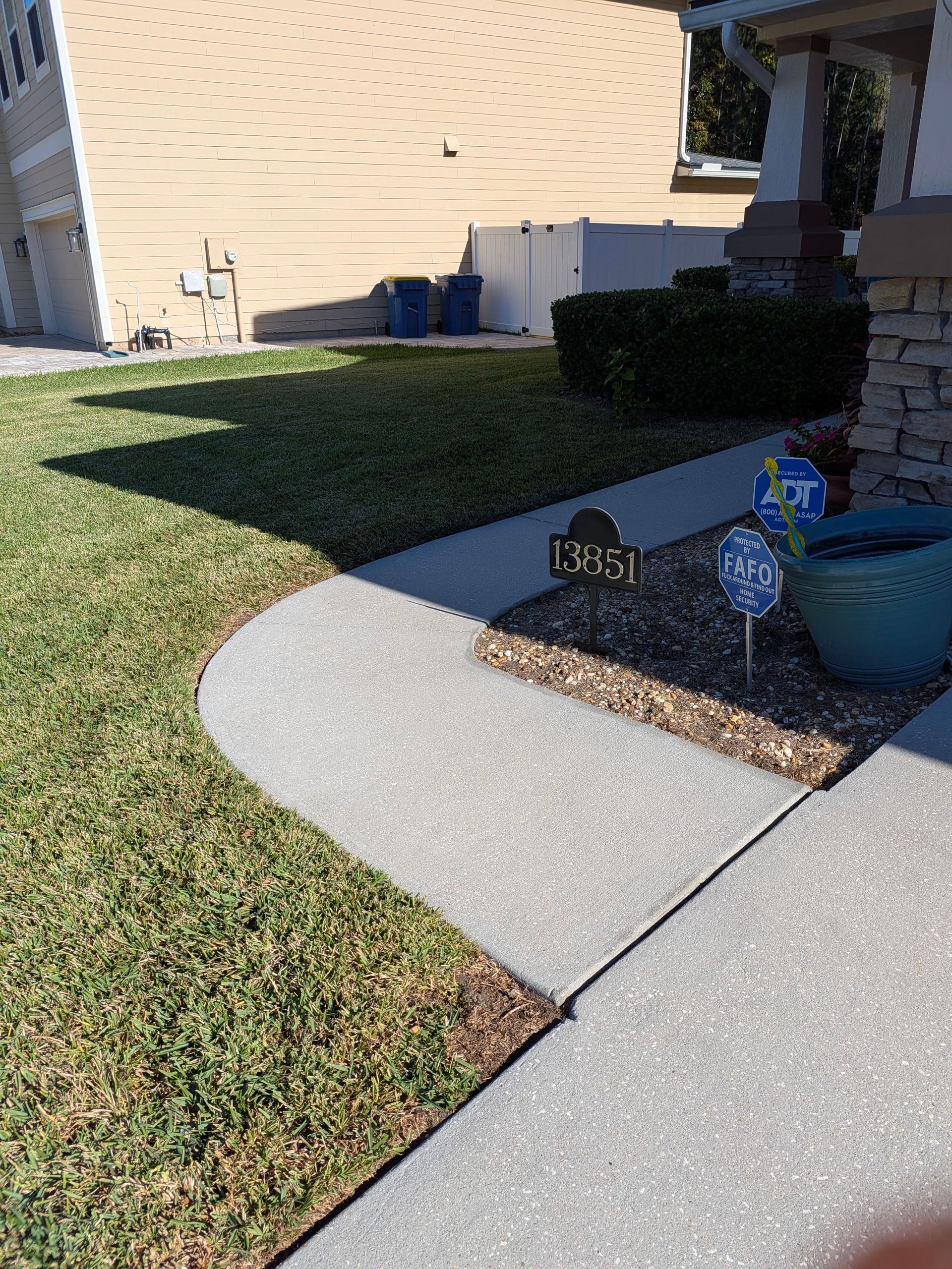 Front walkway with curved concrete path, green lawn, and a house entry with potted plant and house number sign.