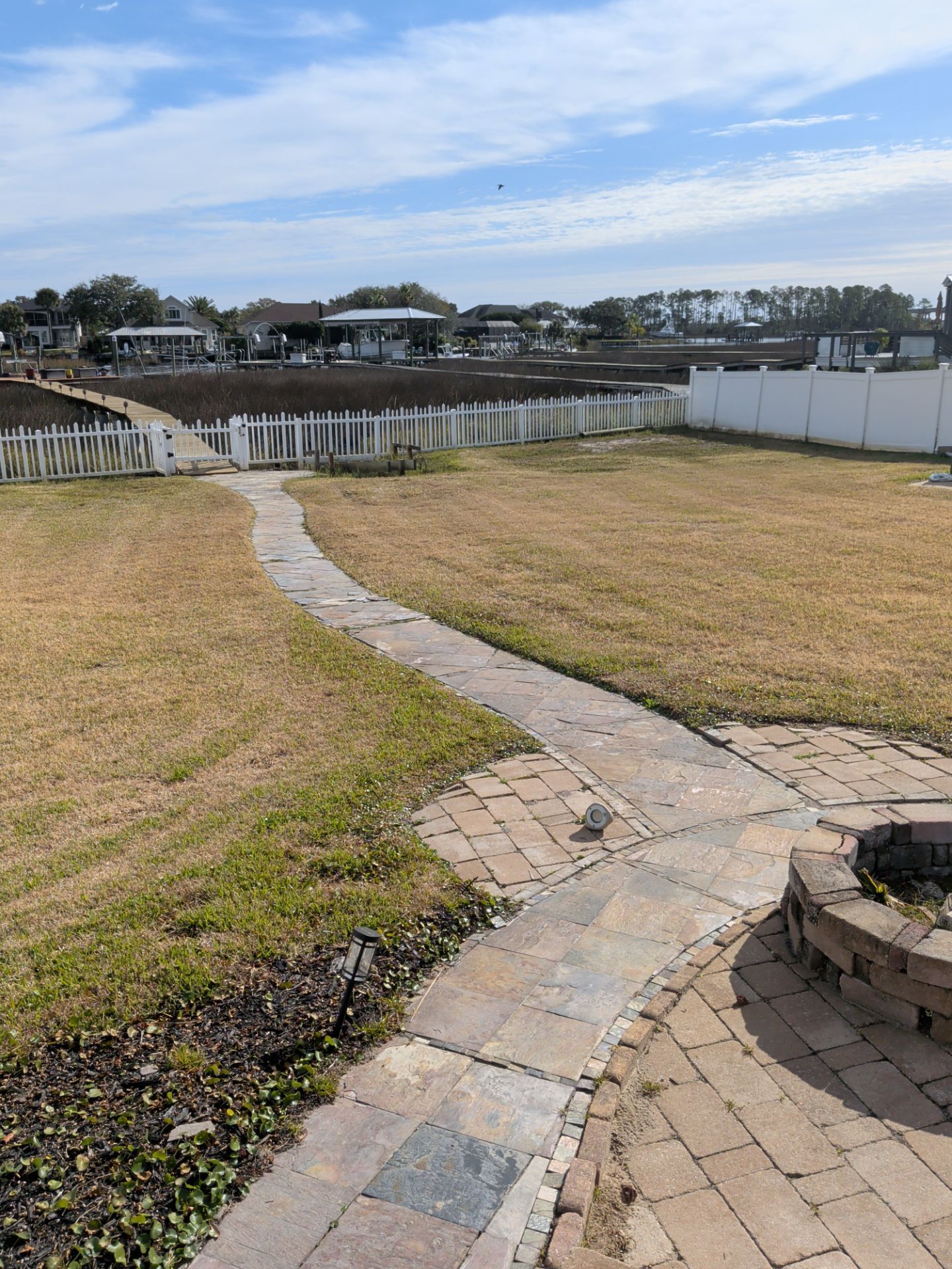 Curved stone path through a grassy yard toward a white fence under a cloudy sky