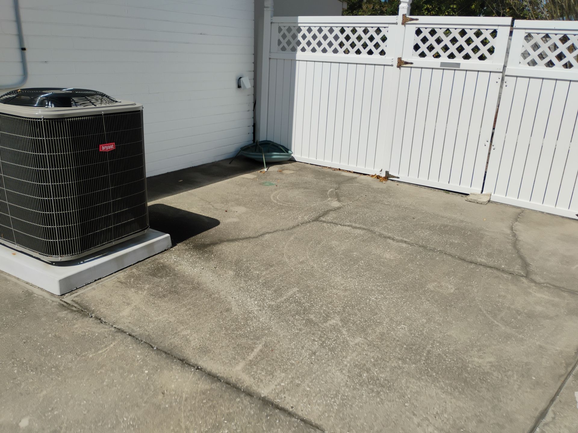 Outdoor concrete patio beside a black air conditioner unit and white vinyl fence.