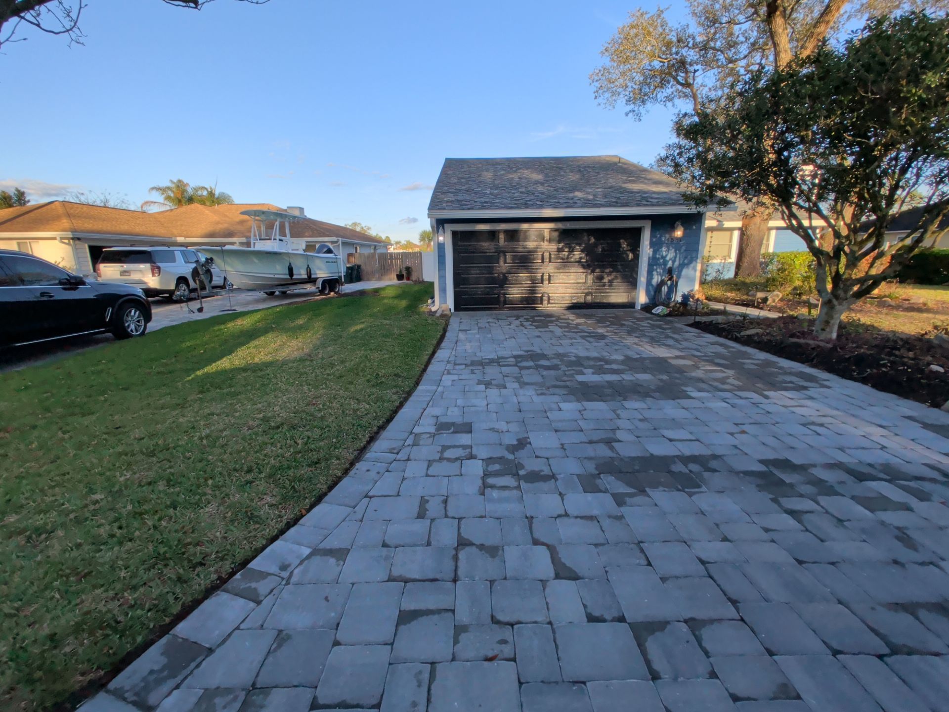 Driveway leading to a two-car garage beside a grassy yard and trees at sunset