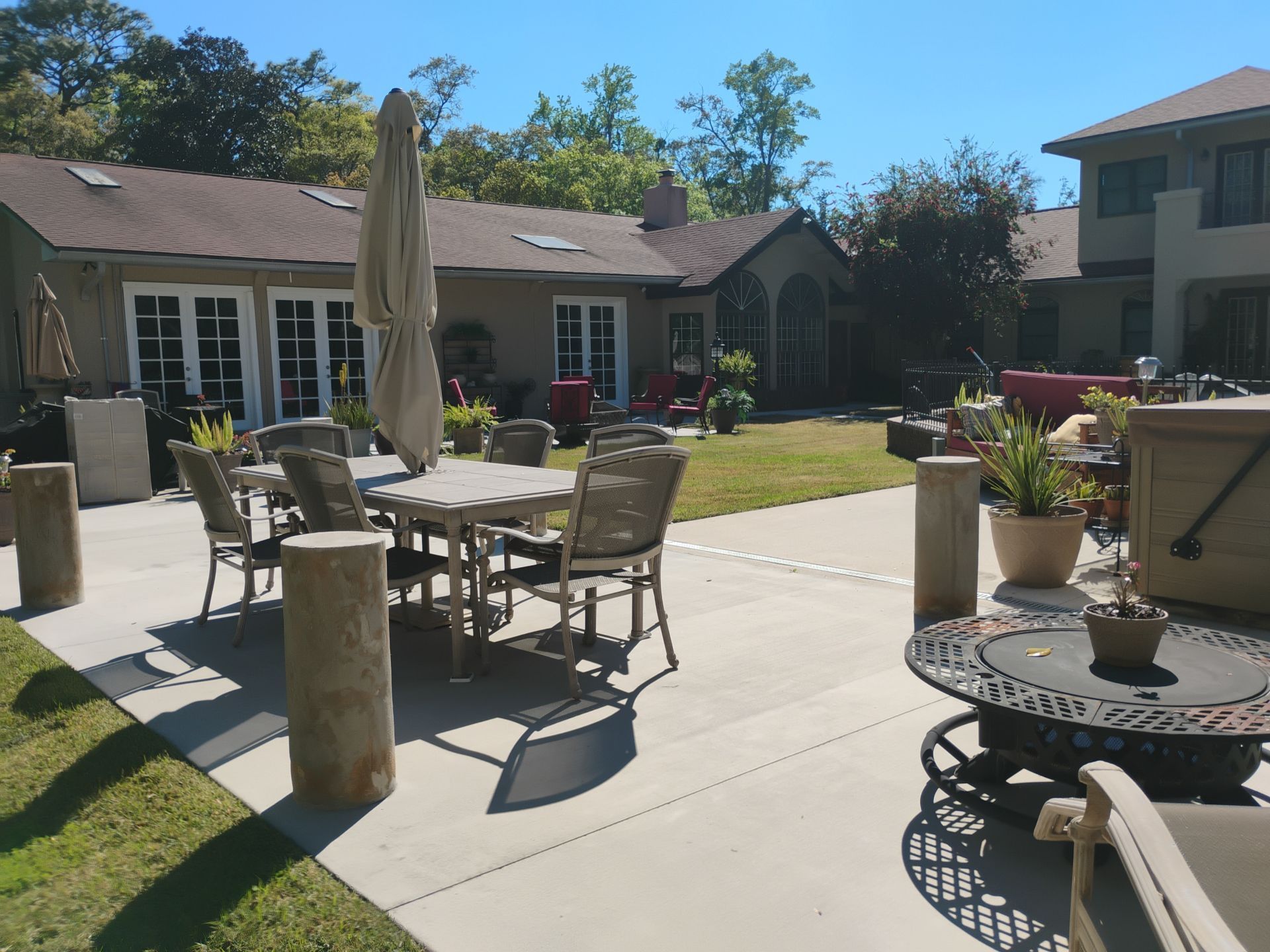 Patio with outdoor dining table, chairs, umbrellas, potted plants, and a lawn beside a house