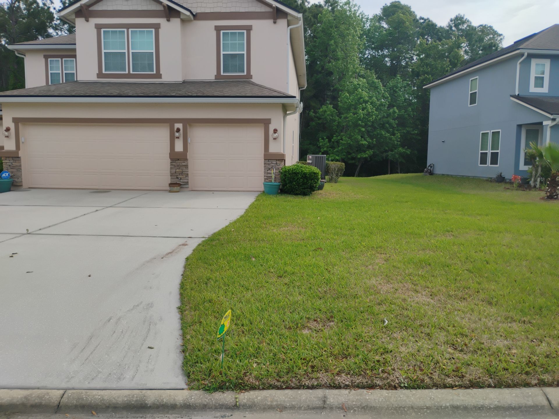 Suburban two-story house with a double garage, driveway, and green lawn beside a neighboring home.