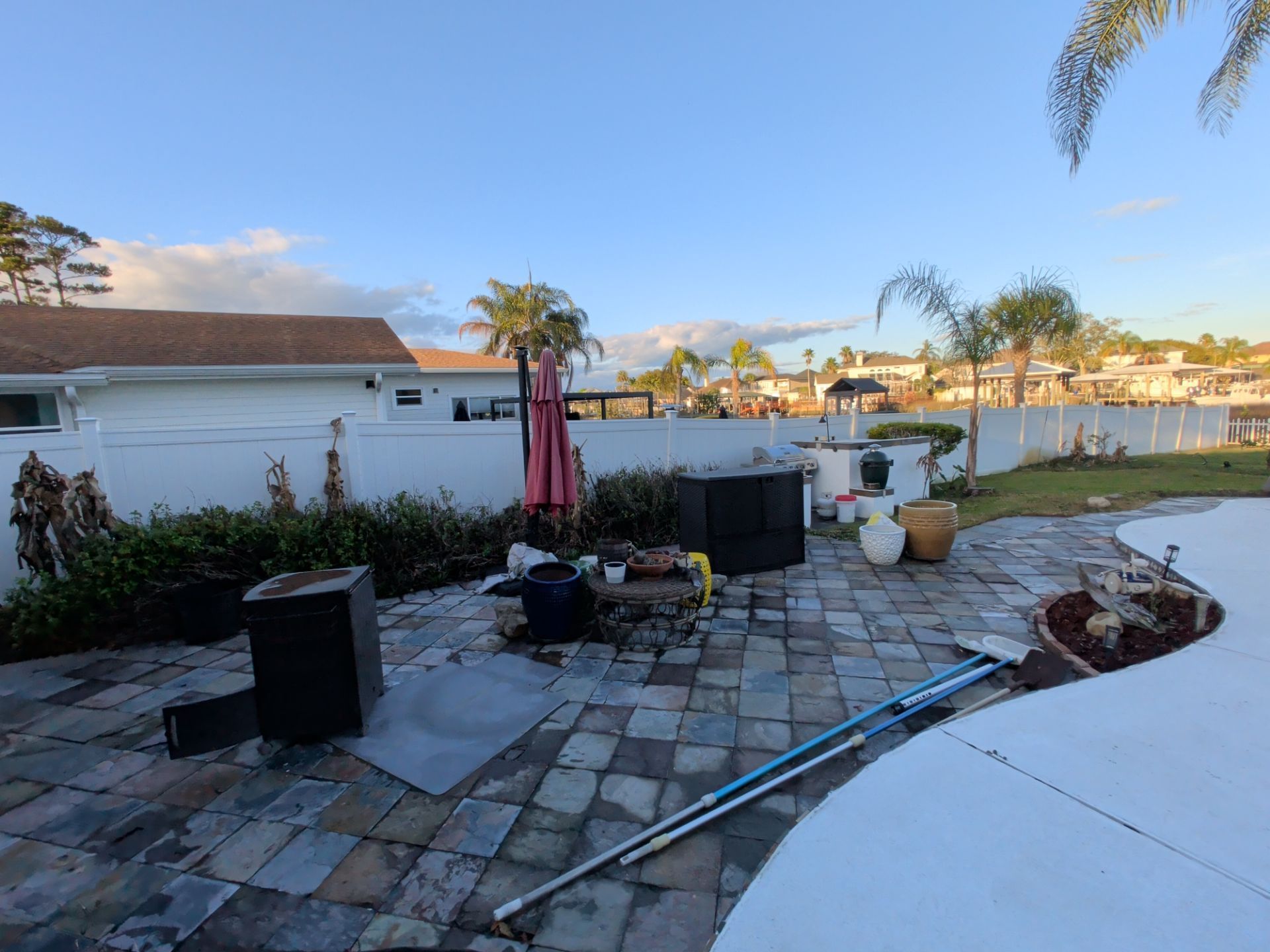 Backyard patio with pavers, potted plants, a folded umbrella, and a lake view at sunset