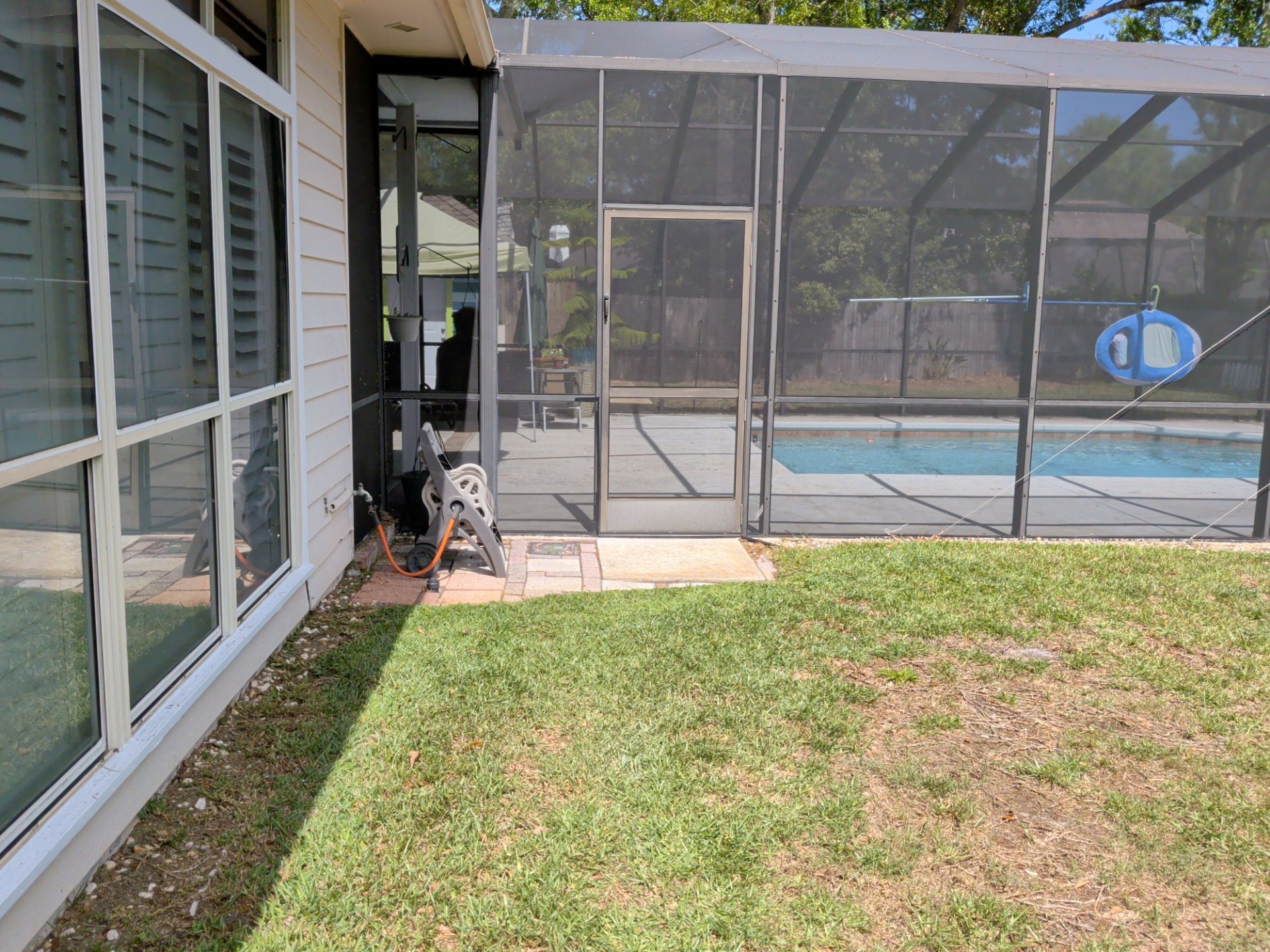 Backyard patio beside screened pool enclosure and grassy yard beside a house