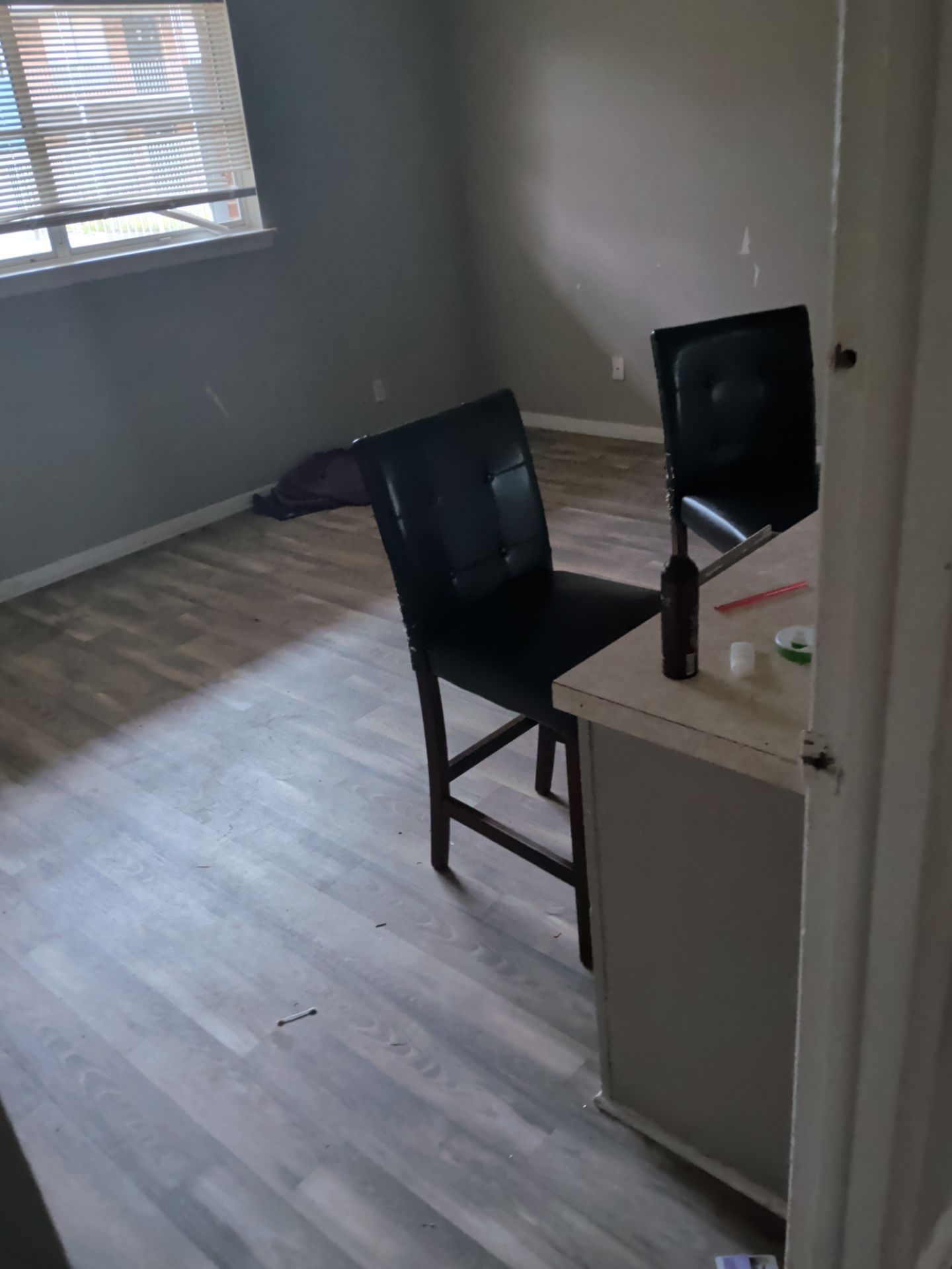 Empty room with gray walls, wood flooring, a desk, and two black chairs near a window.
