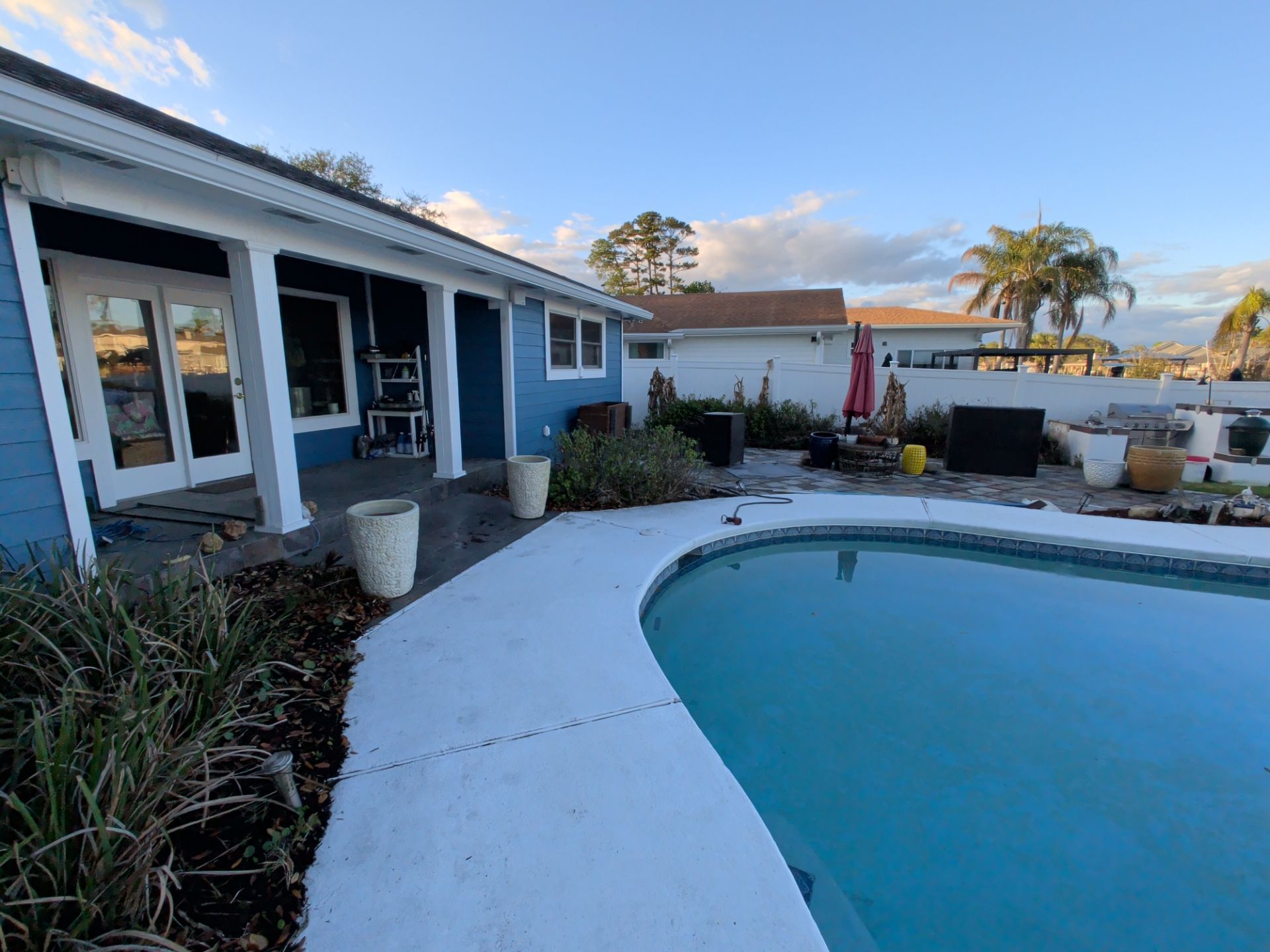 Blue house patio with a curved pool and ocean view at sunset
