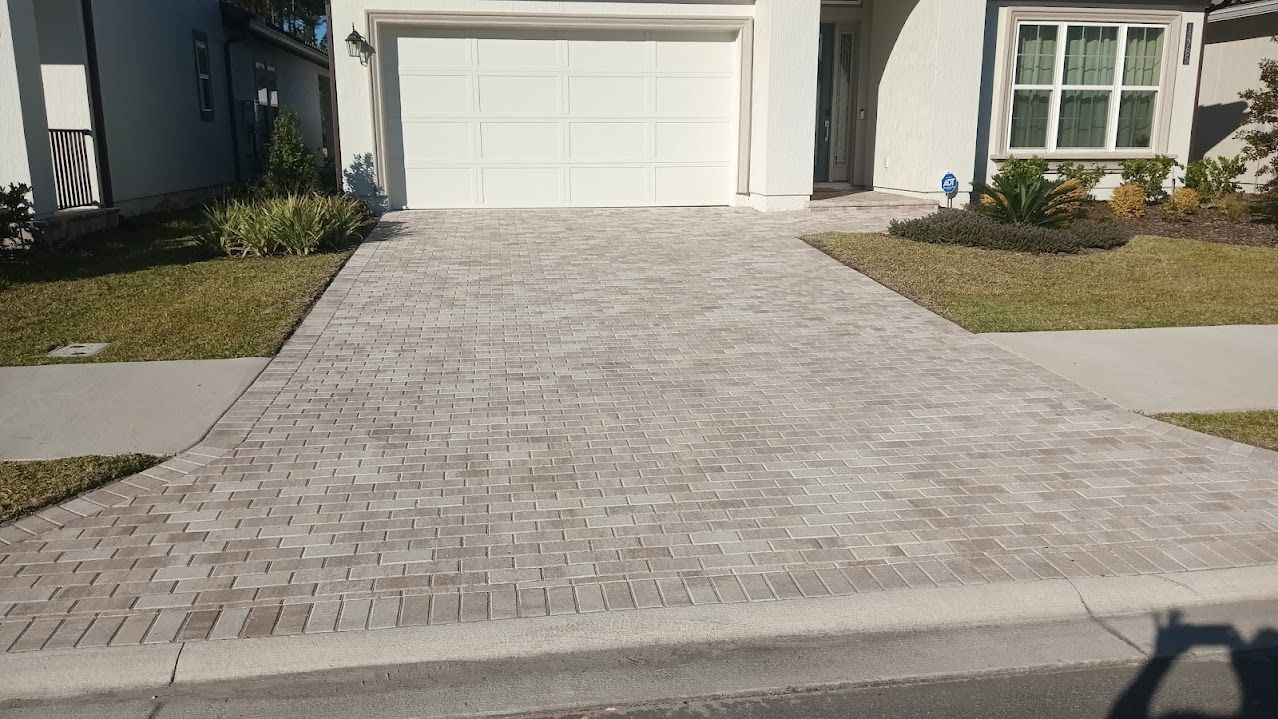 Driveway paved with interlocking bricks leading to a white garage door; grass on either side.