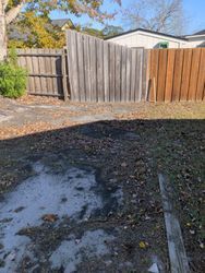Backyard with a damaged, varied wooden fence and fallen leaves on the ground.