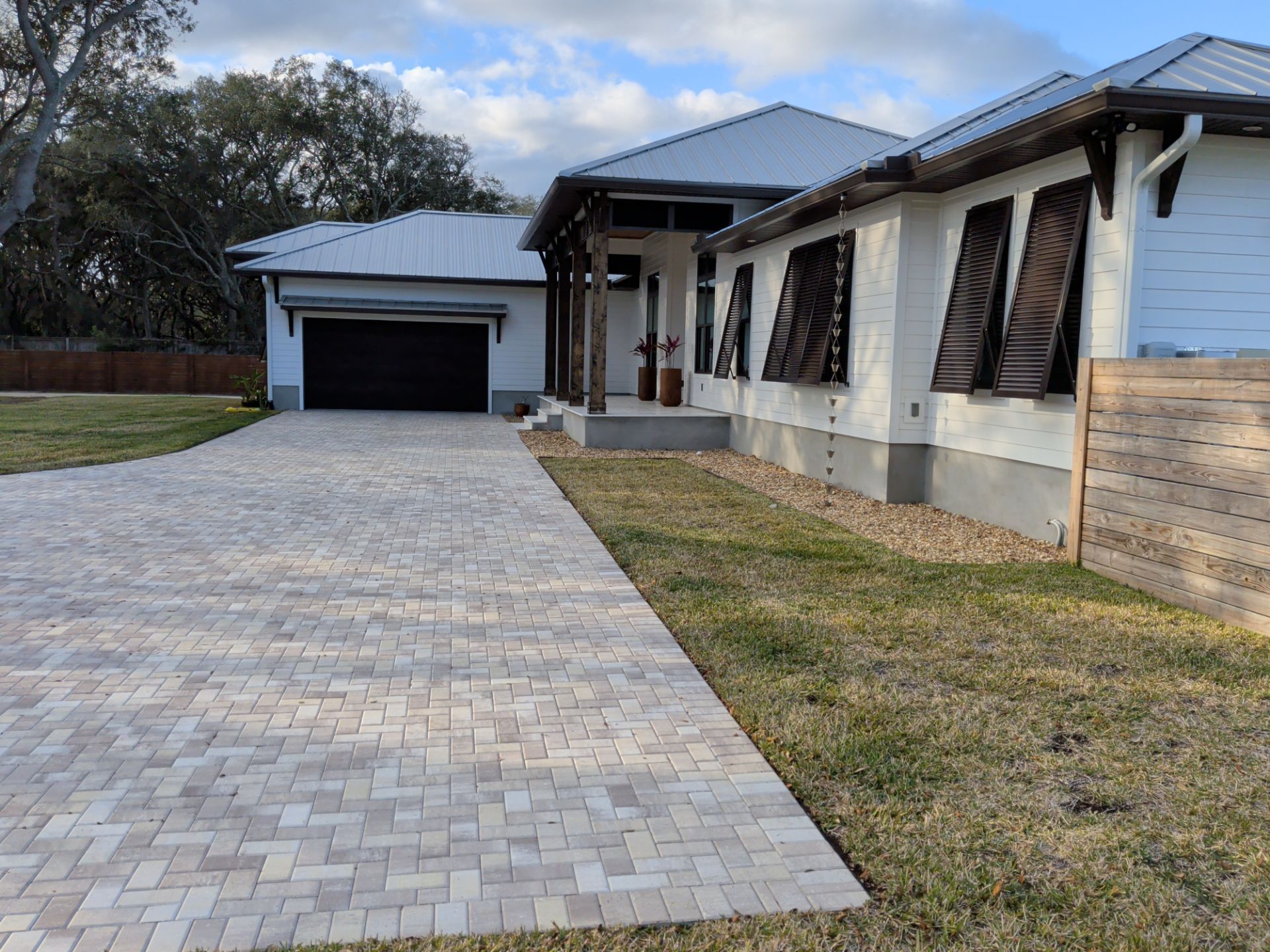 Long paved driveway leading to a white house and detached garage under a cloudy sky