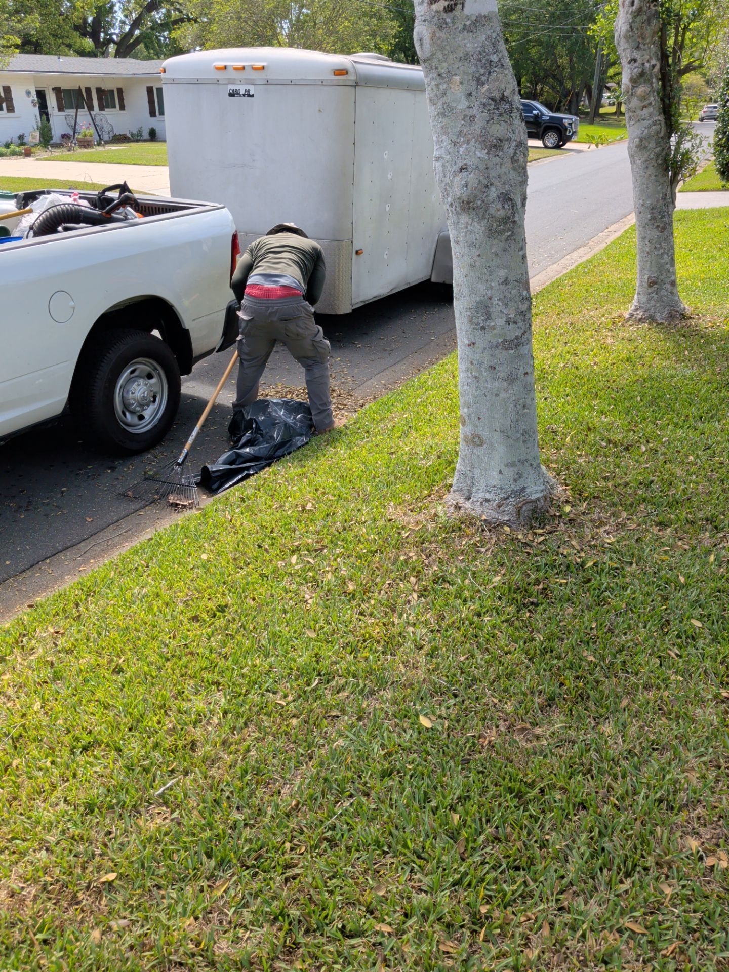 Person pushing a white trailer hitched to a white pickup truck on a suburban street.