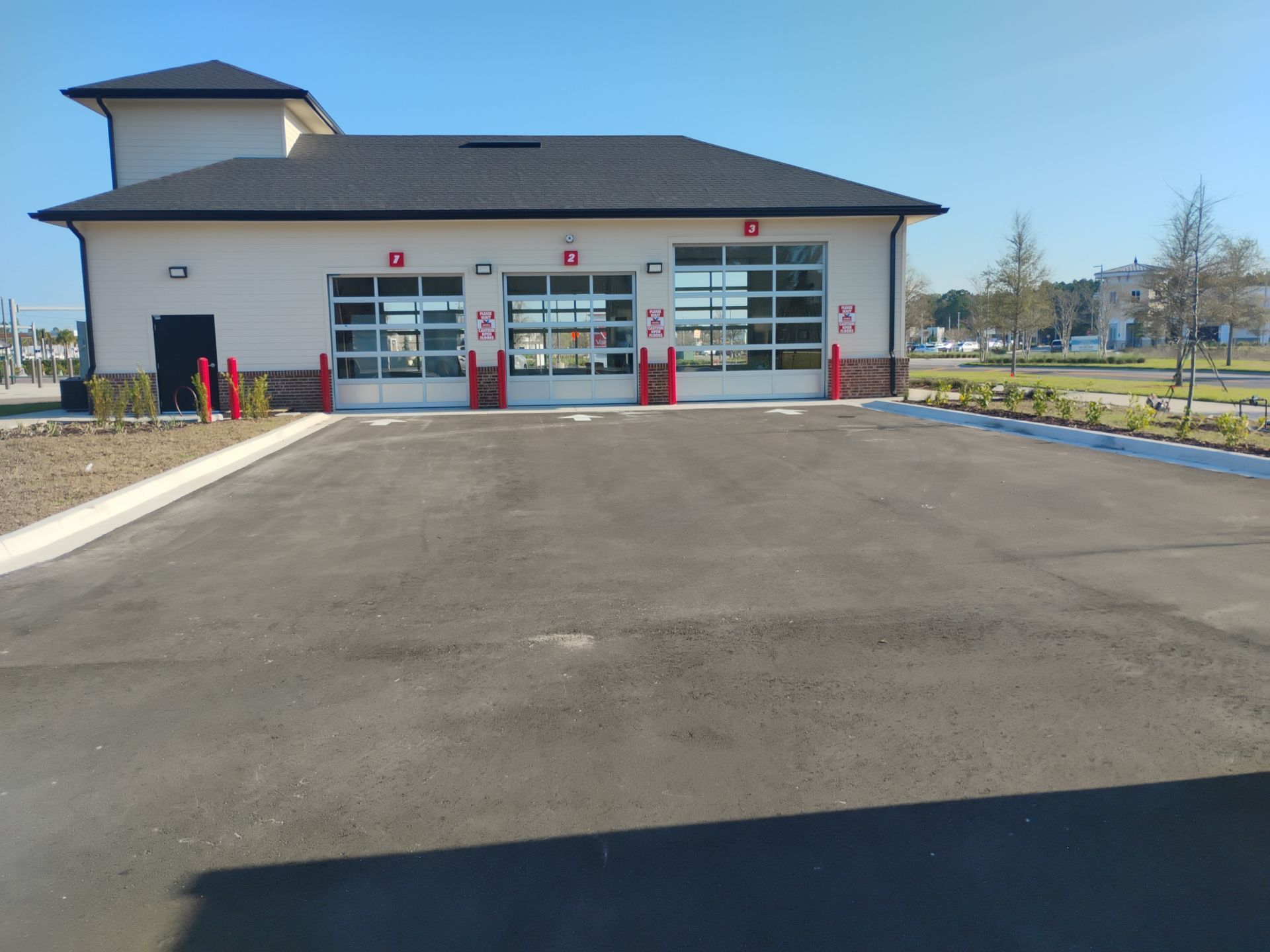 Fire station with three garage bays and a wide asphalt driveway under a clear blue sky