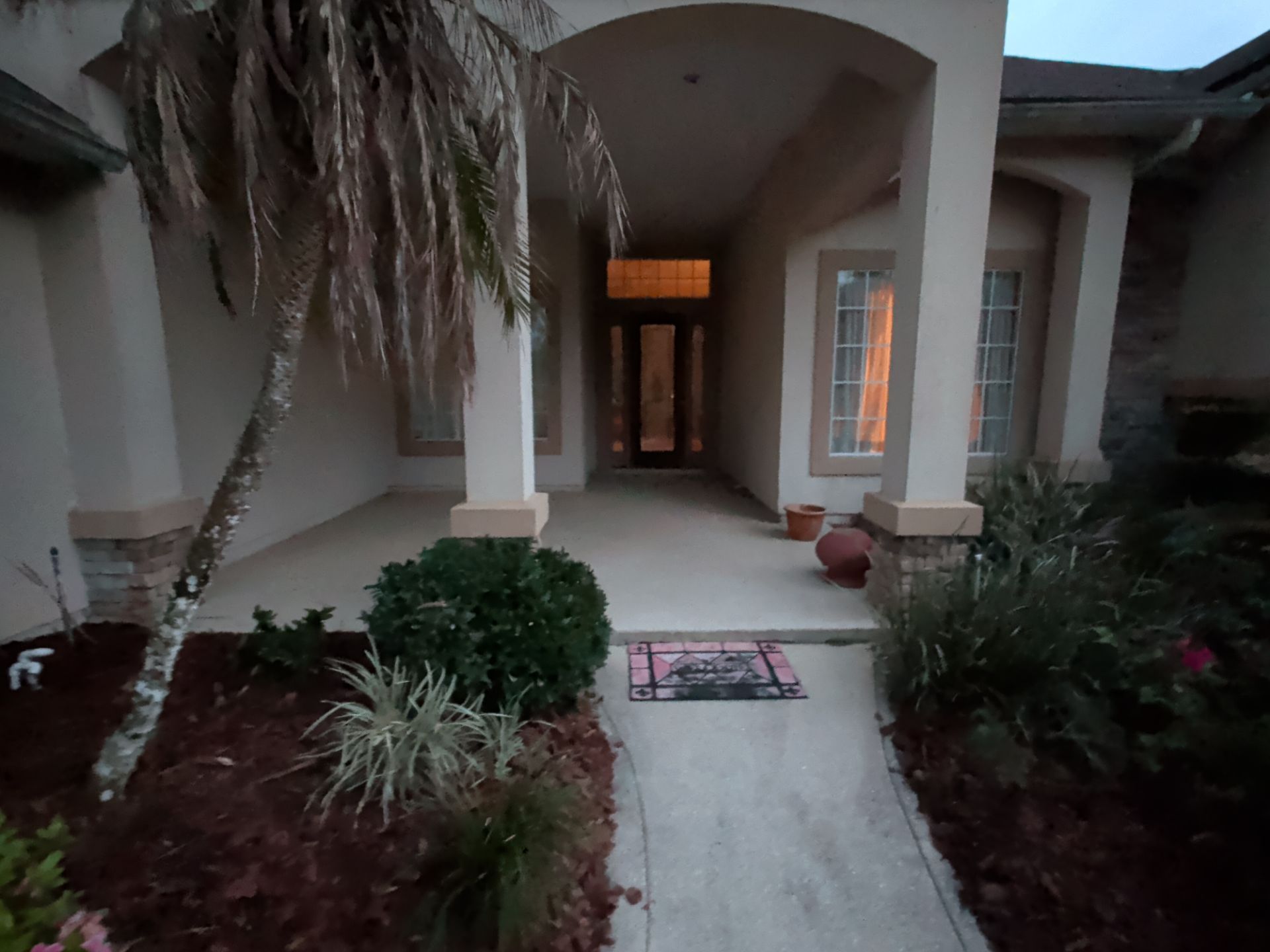 Front entry walkway leading to a covered porch with arches, potted plants, and warm interior light