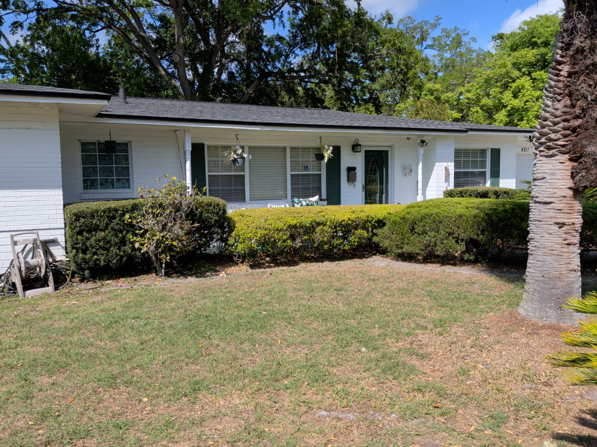 Single-story white house with porch, trimmed hedges, and a front lawn under a clear blue sky