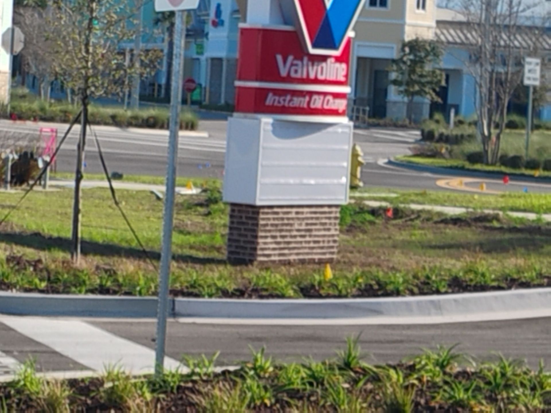 Valvoline service center sign beside a roadside landscaped island, with cars and buildings in the background