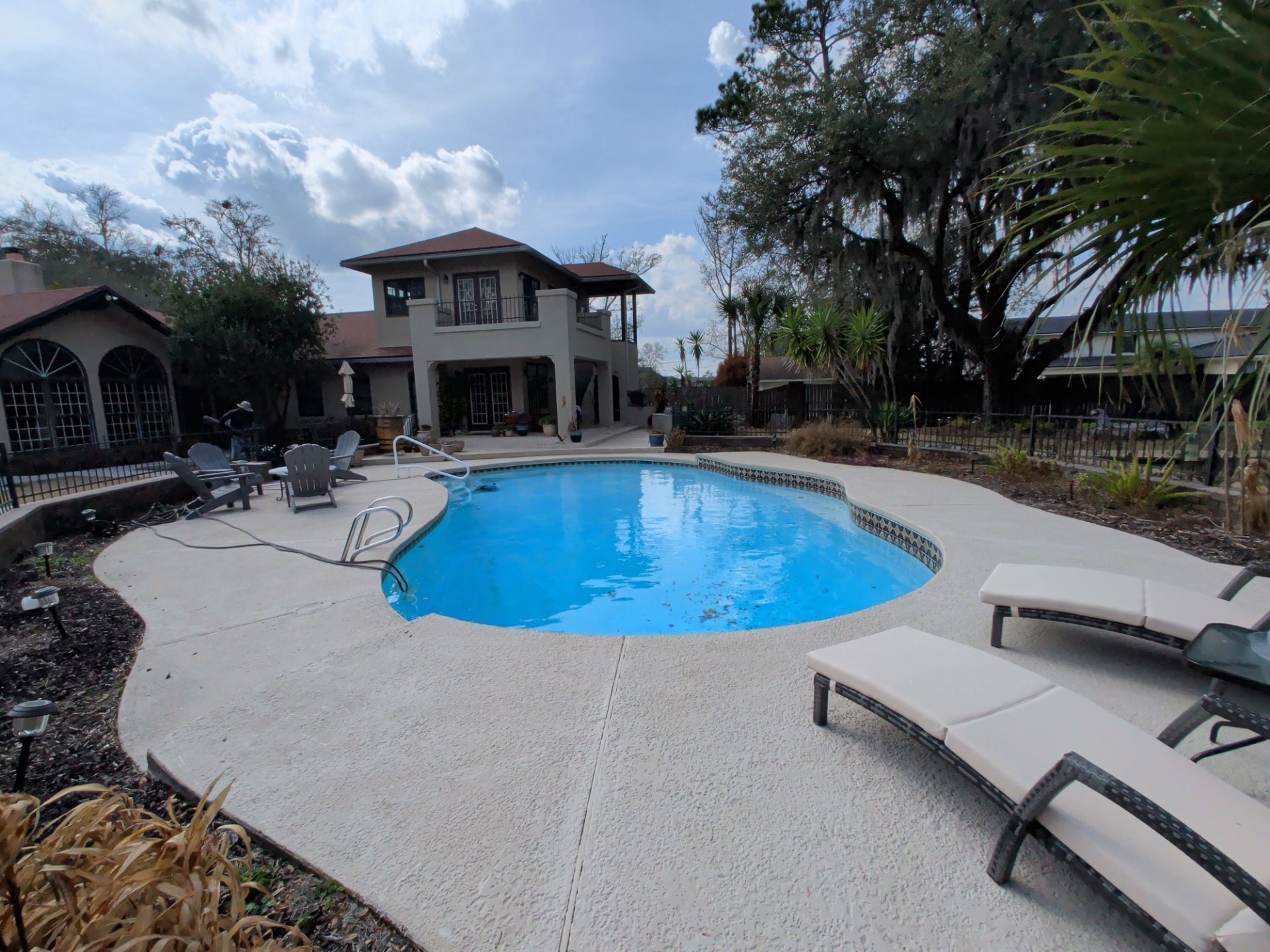 Backyard swimming pool with lounge chairs, patio, and trees under a partly cloudy sky