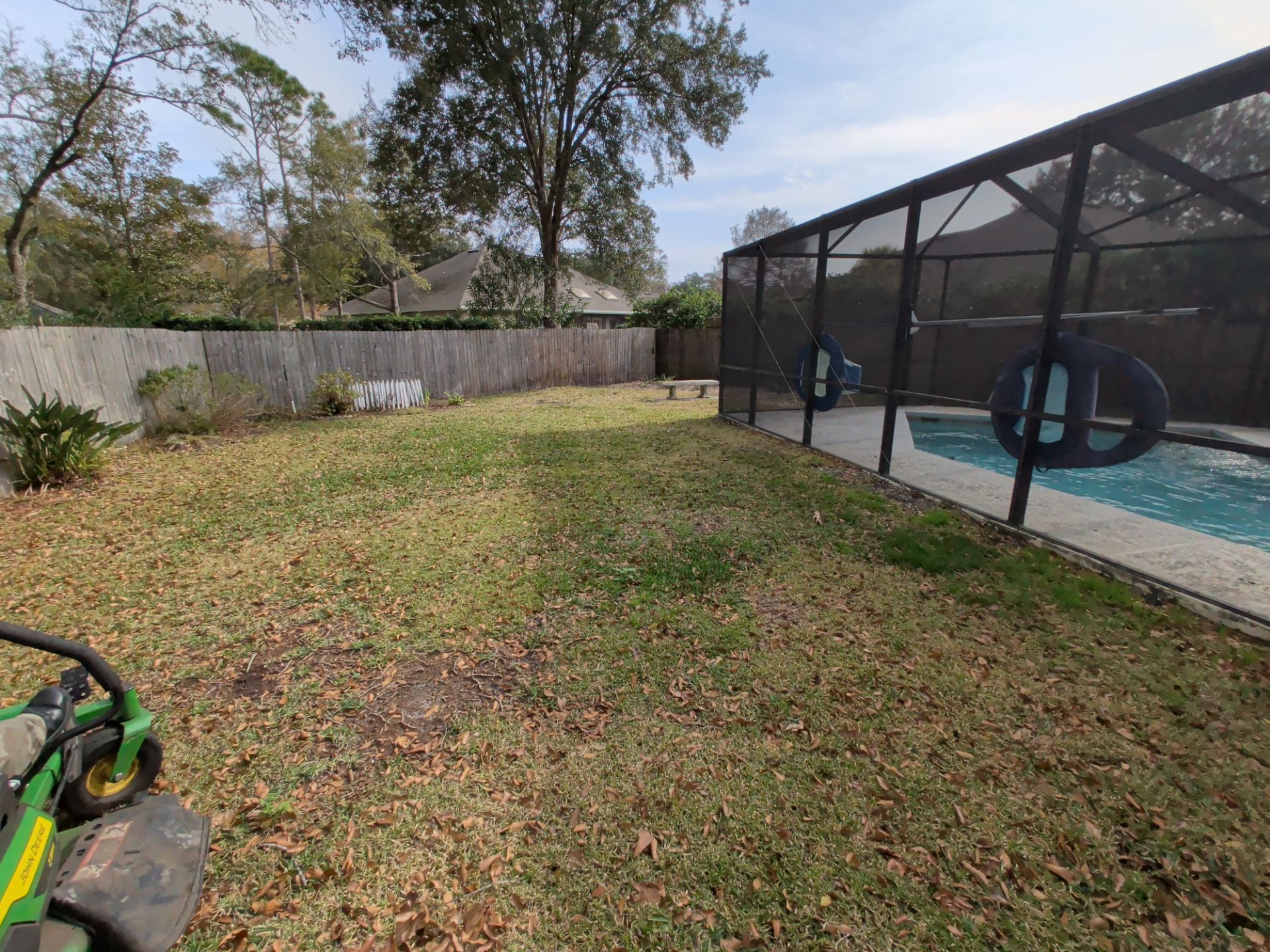 Backyard lawn beside a screened-in pool, with trees and a fence in the background.