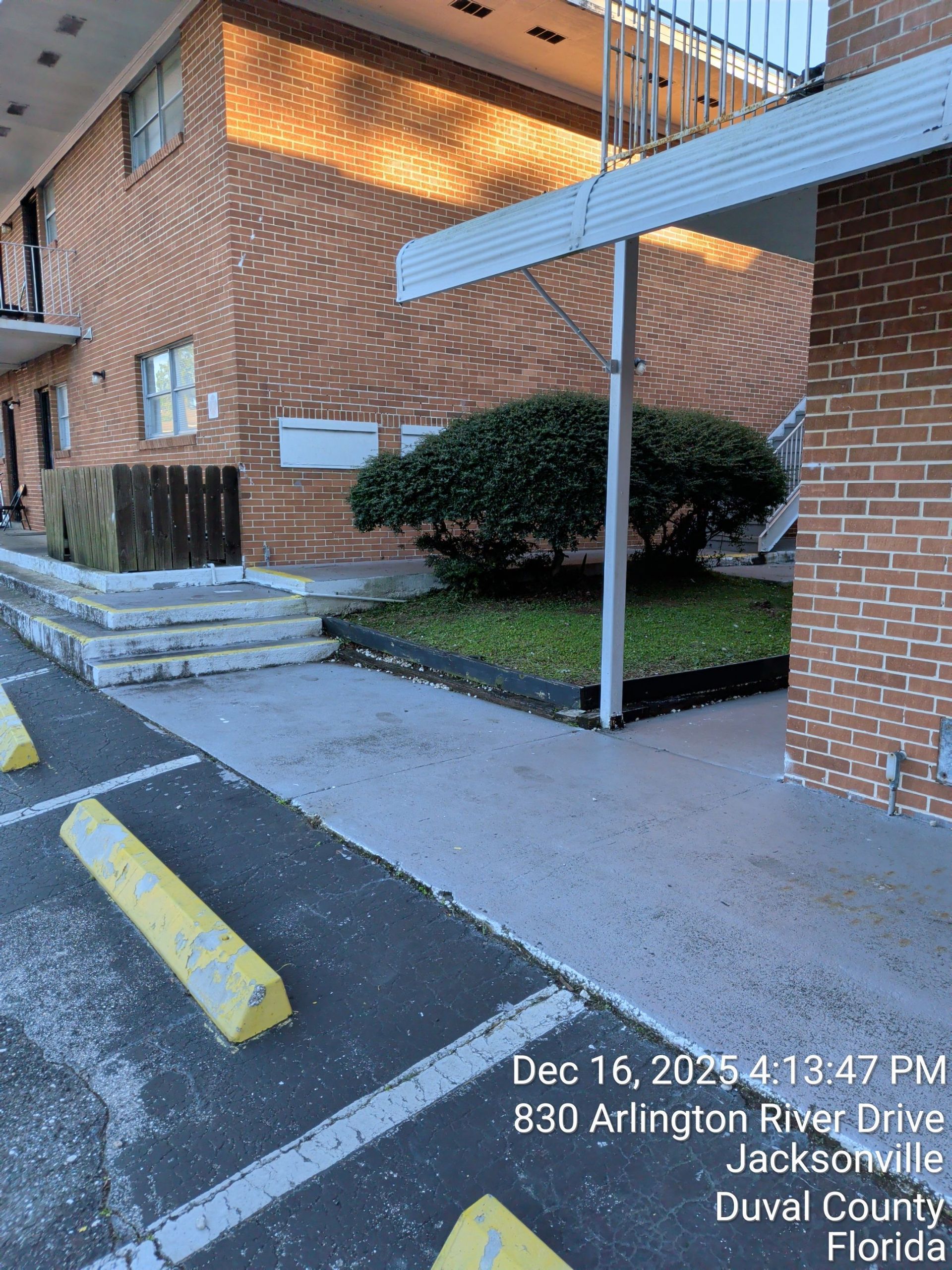 Brick apartment entrance with ramp, canopy, parking lot, and yellow curb stop in daylight